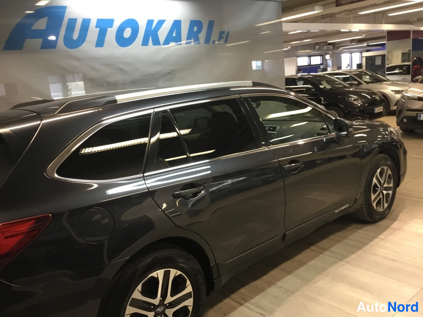 Sivulta: Sivukuva tummanharmaasta Subaru Outback -asema-autosta, oikea kylki näkyvissä Autokari-tiloissa.