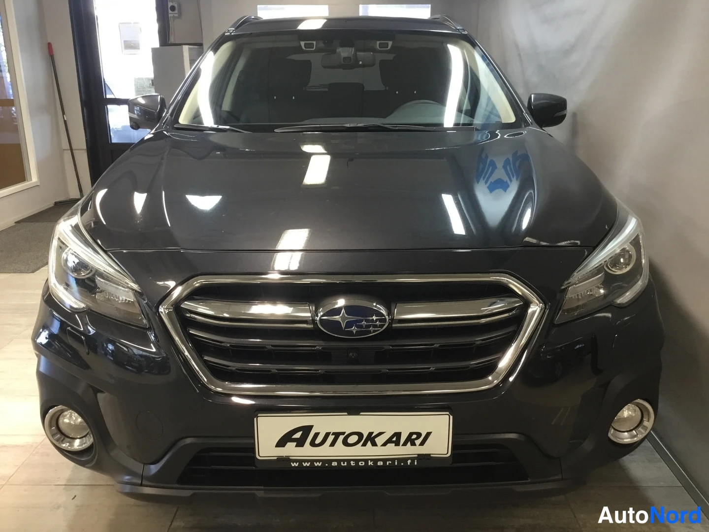 Edestä: Front view of a dark Subaru station wagon in a showroom