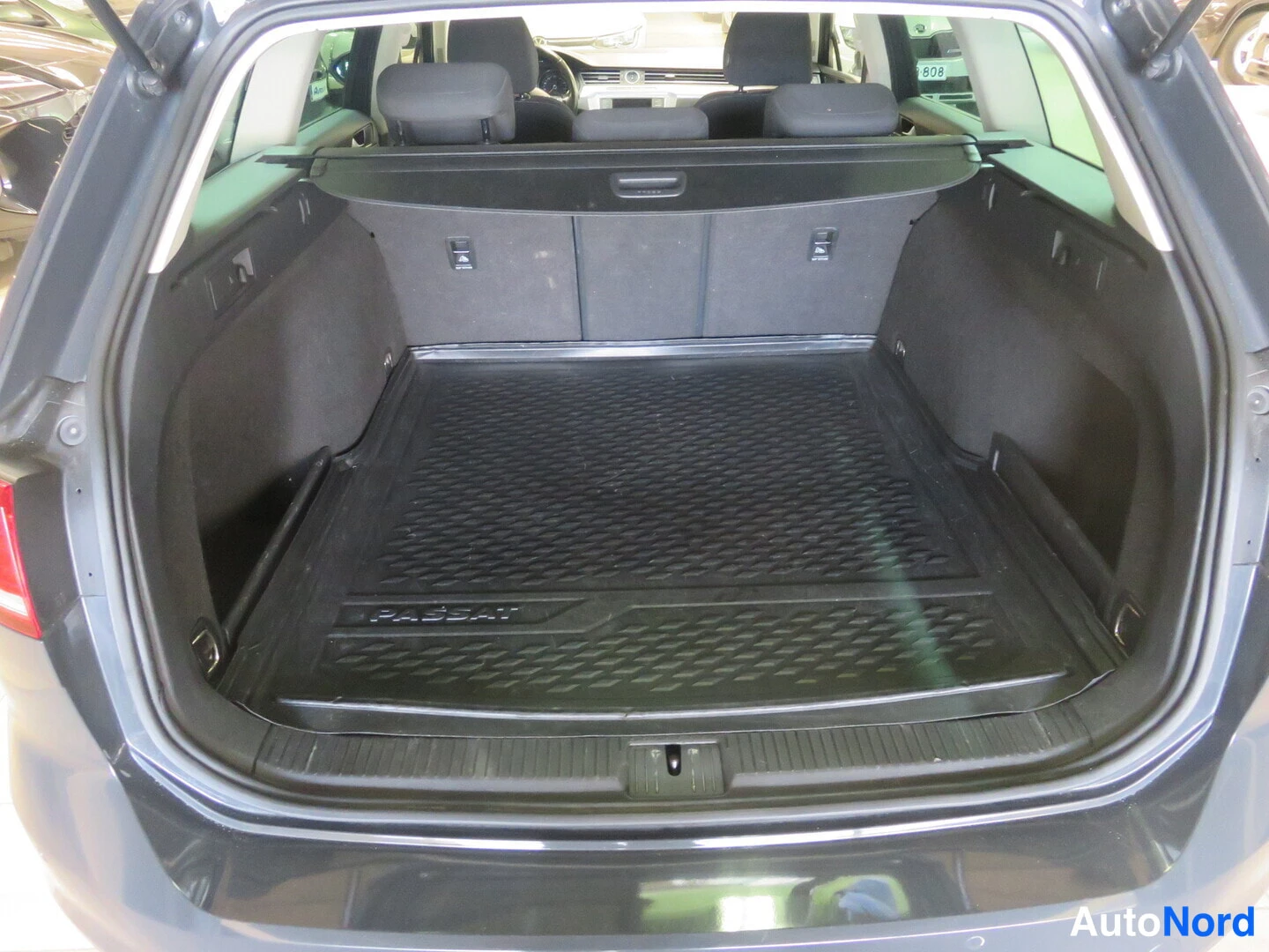 Tavaratila: View of the vehicle's cargo area with rear seats folded or removed. A black rubber mat with 'PASSAT' embossed text covers the floor.