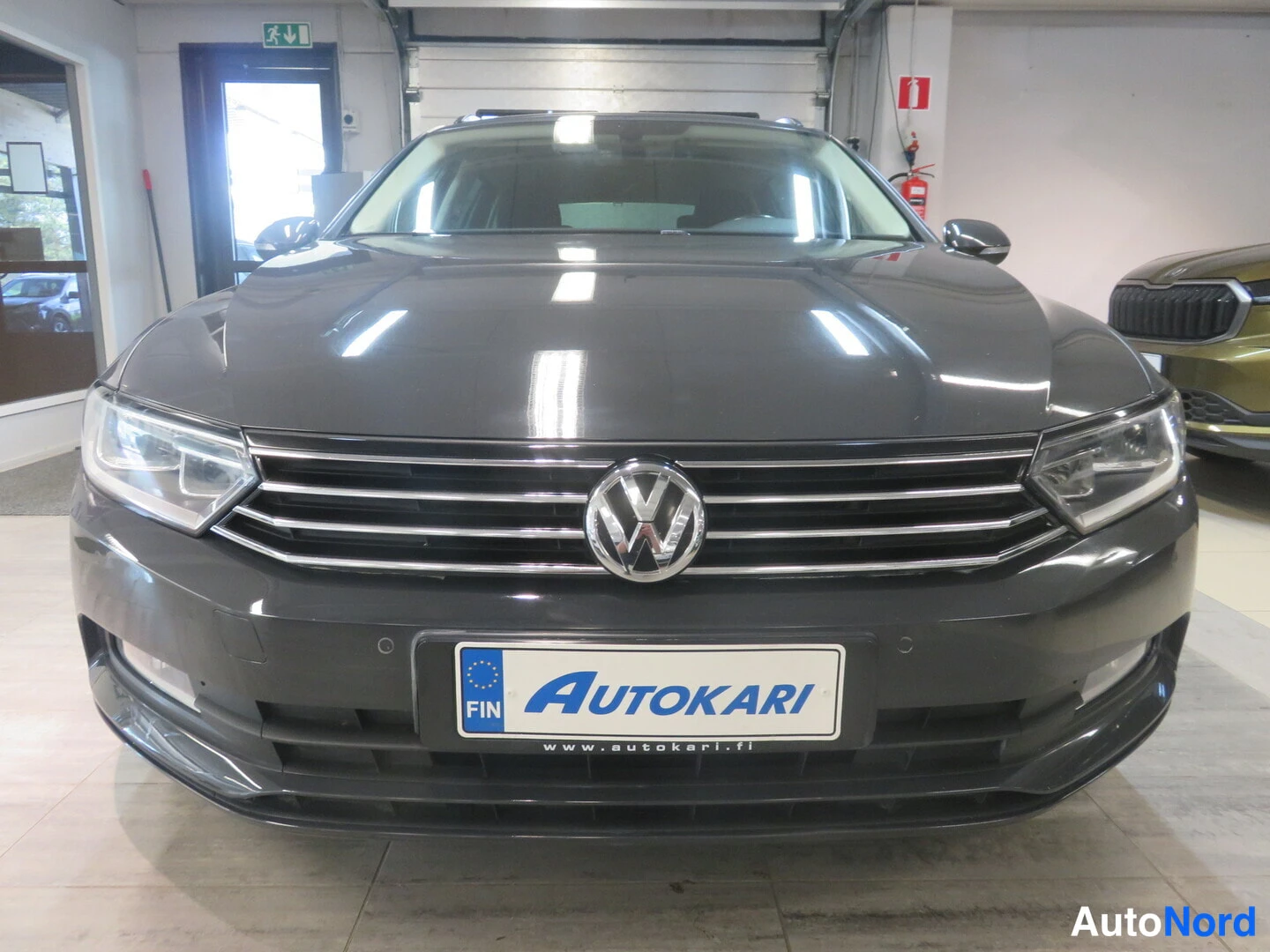 Edestä: Volkswagenin etupää tummassa värisävyssä, AutoKari-kilpi etupuskurissa.