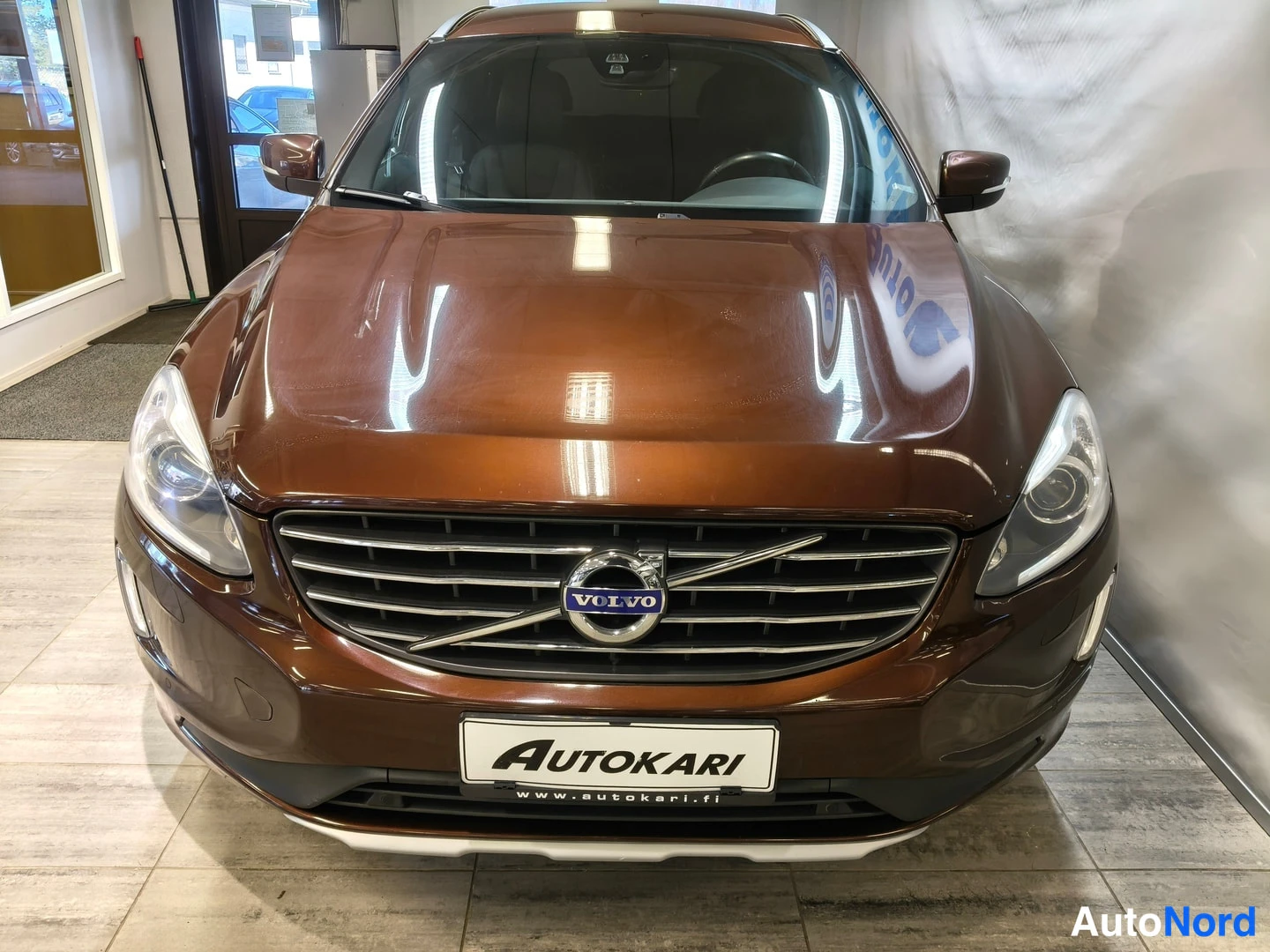 Edestä: Front view of brown Volvo showing grille with logo and headlight design in showroom.