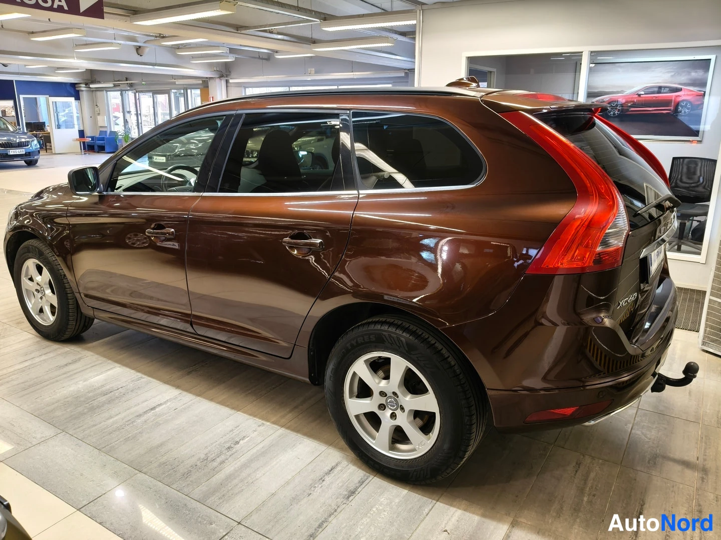 Takaviisto: Rear three-quarter view of brown Volvo with tow bar, red tail light, and silver roof rails.