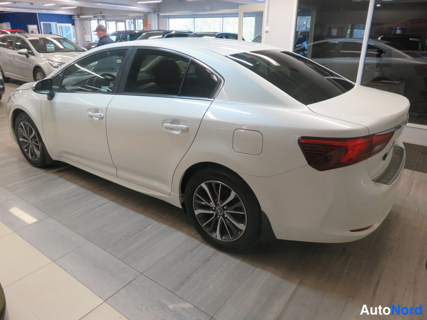 Takaviisto: Valkoinen Toyota Avensis -sedan takaviistosta myymälässä.
