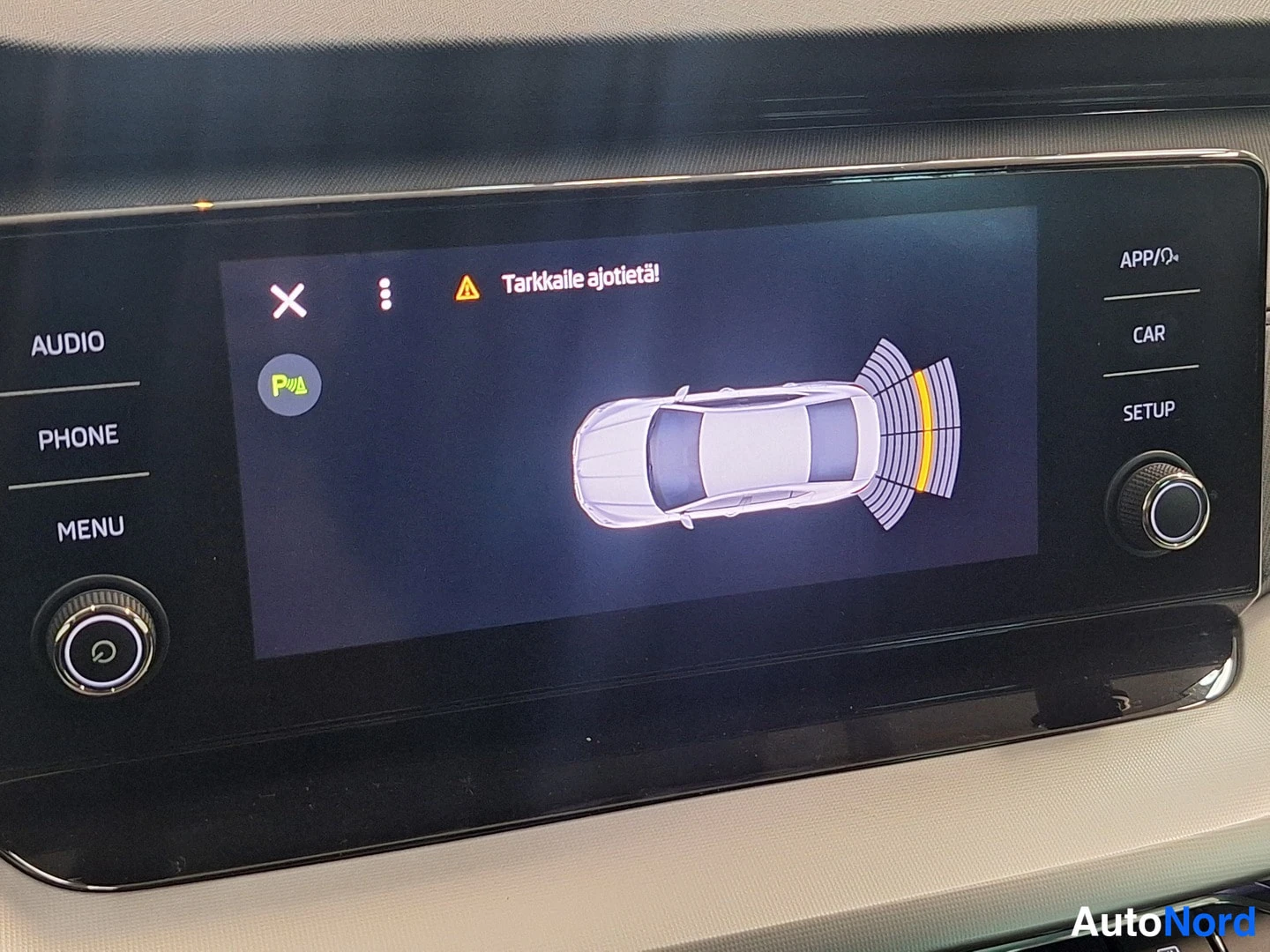 Muu: Kojeisteen infotainmentnäyttö, jossa pysäköintianturin auto ylhäältä -visualisointi ja varoitus Tarkkaille ajotietä!. Napit AUDIO, PHONE, MENU, APP/, CAR ja SET