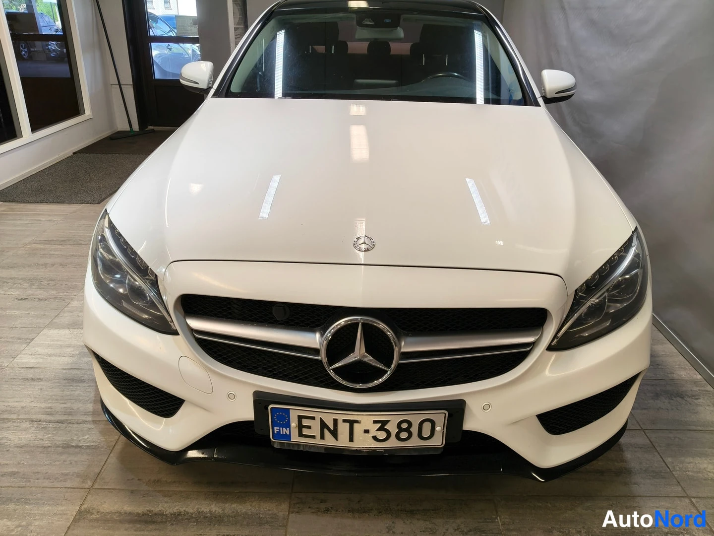 Edestä: Valkoisen Mercedes-Benz C-sarjan sedanin suora etunäkymä, Mercedes-tähti etusäleikössä, rekisterikilpi.