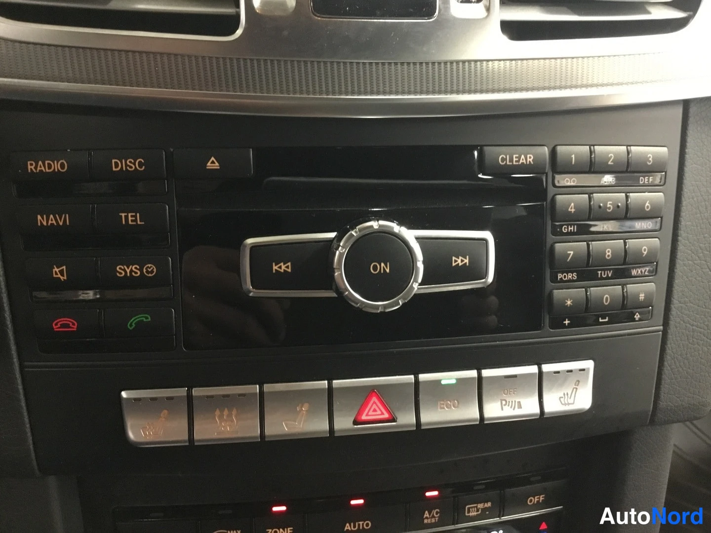 Muu: Mercedes-Benzin kojelaudan keskirivi: radio- ja navigointipainikkeet, COMAND-ohjainkiekko, numeronäppäimistö sekä istuttimien lämmitys- ja ECO-painikerivi.