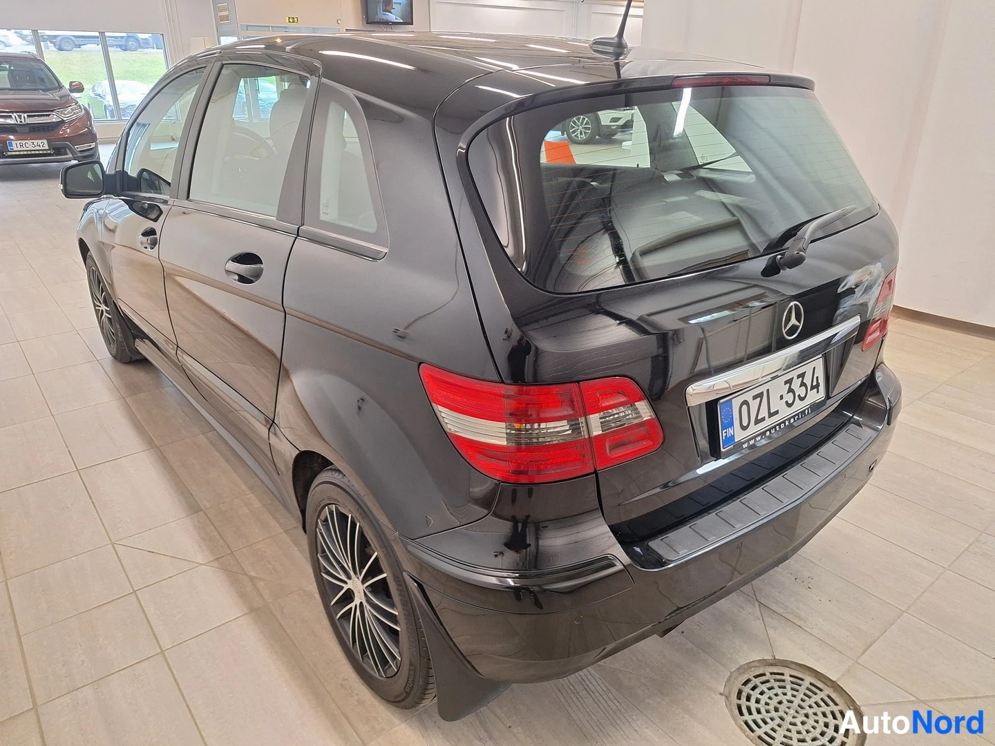 Takaviisto: Musta Mercedes-Benz B 180 takaneljännesvasen, perä ja oikea sivu näkyvissä, rekisteritunnus.