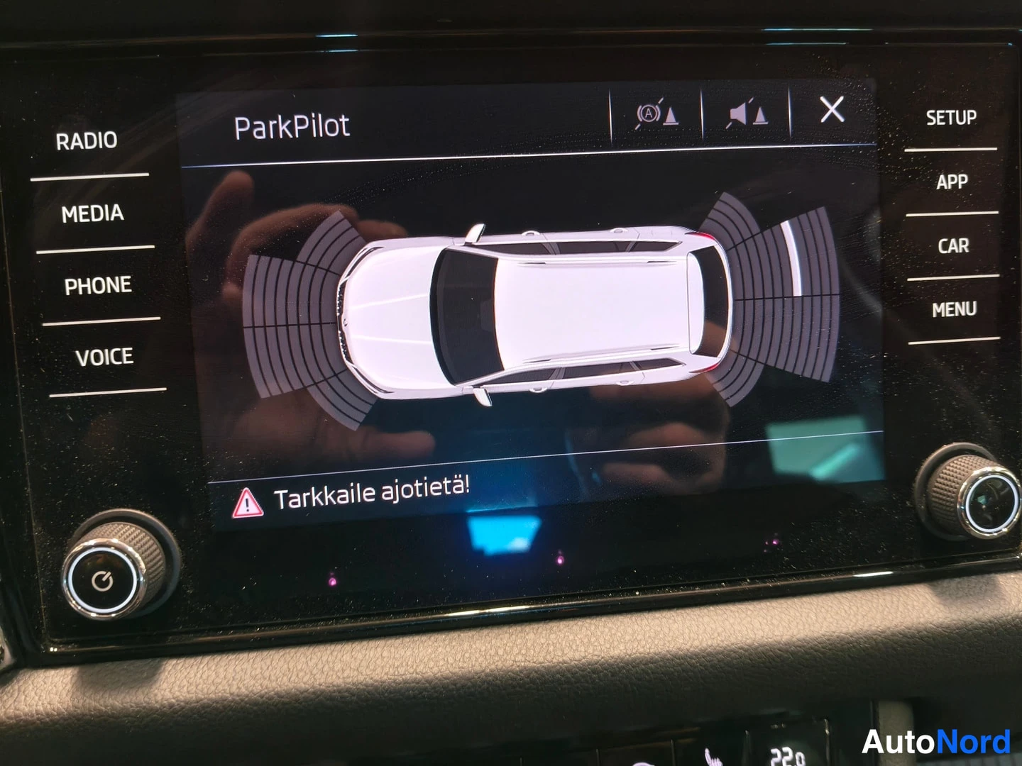 Muu: Keskikonsolin näyttö ParkPilot-törmäysvaroitusnäkymässä, jonka kuvassa on auton yläkuvapohja ja varoitus Tarkkaile ajotietä!.