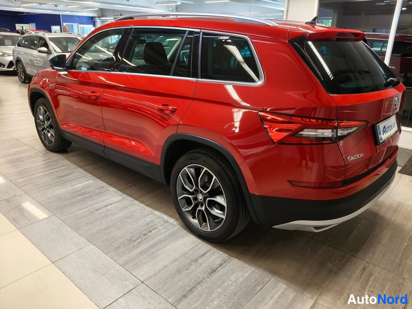 Takaviisto: Punainen Skoda Kodiaq takakulmasta vasemmalta; takavalot, ŠKODA-merkki ja kattokaiteet näkyvät showroomin lattiassa.