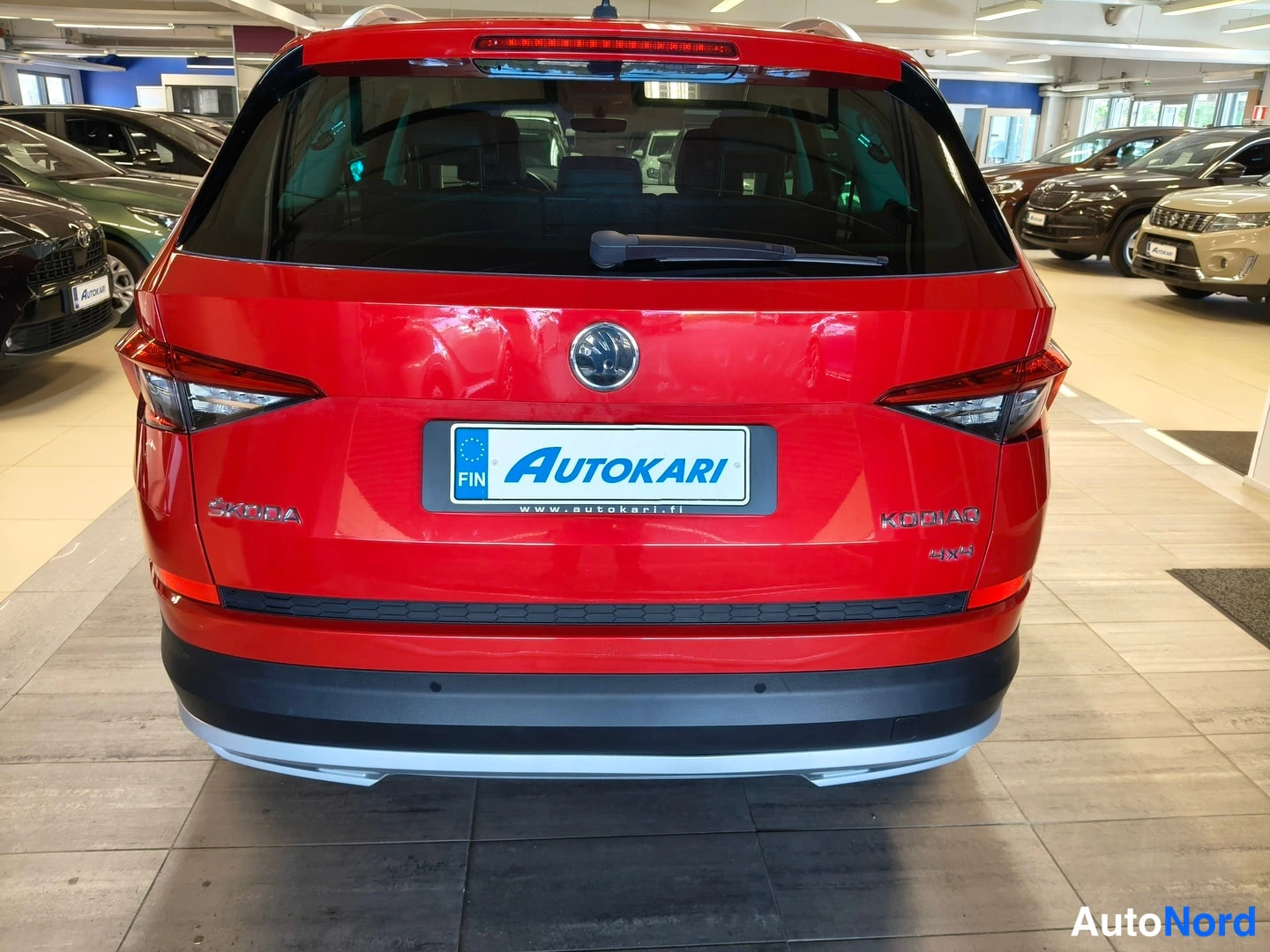 Takaa: Punaisen ŠKODA Kodiaq -autojen takanäky myymälässä, rekisterikilven paikalla AUTOKARI-tunnus.