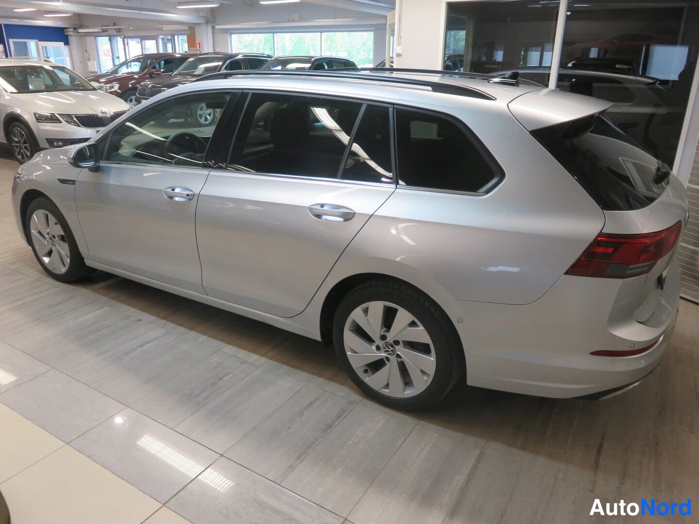 Takaviisto: Hopeanvärinen farmariauto sivusta takaa kuvattuna autosalissa.