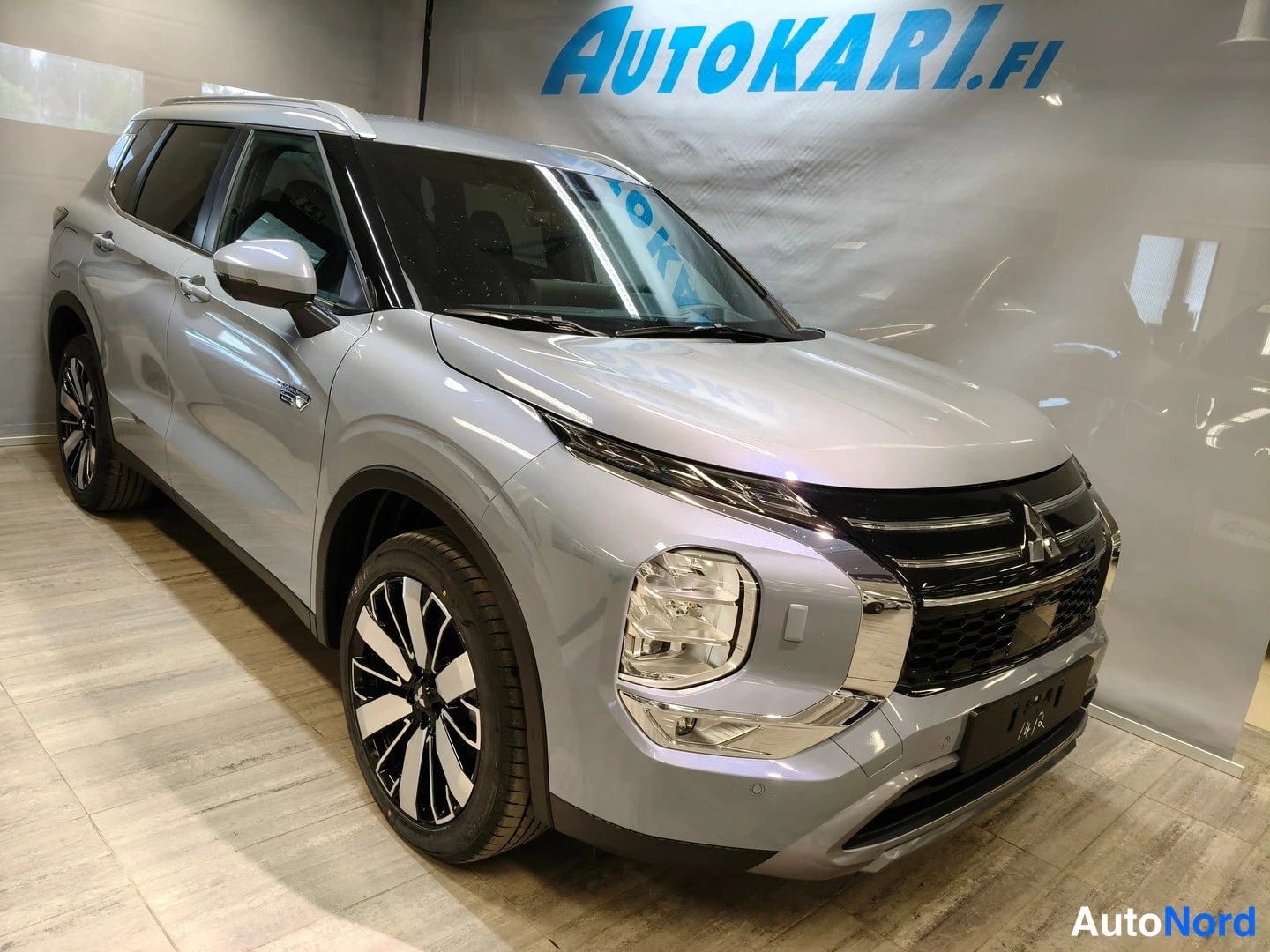 Etuviisto, nokka oikealle: Matala edellinen kolmanneskuva hopeisesta SUV:sta näytettävänä sisätiloissa. Auto on kääntynyt hieman kameraan päin oikealle. Kuvassa näkyy auton etuosa