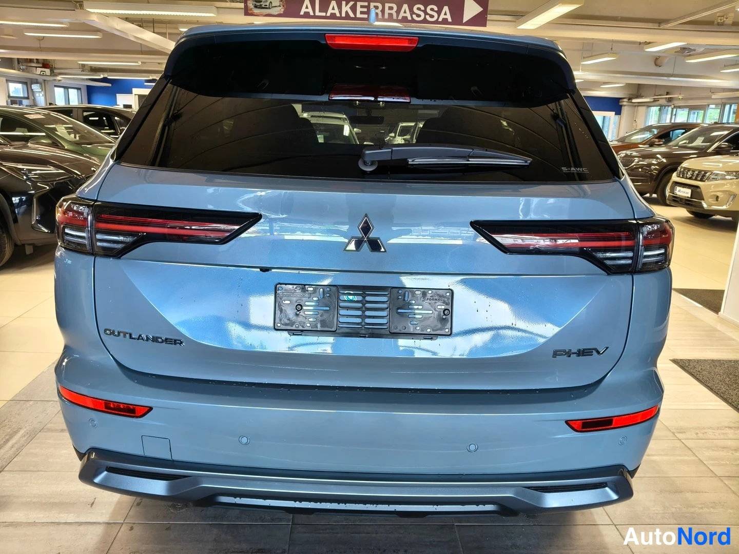 Takaa: Sinertävänharmaan Mistubishi Outlanderin takanäky myyntihallissa, PHEV-tunnus ja Mitsubishi-merkki näkyvät.