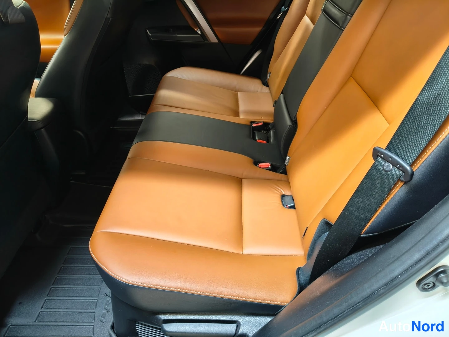 Yksityiskohta: Auton takapenkki, ruskean ja mustan nahkaverhoilu, kolme turvavyönsolkea ja Isofix-kiinnikkeet näkyvät, musta lattiamatto eteen.