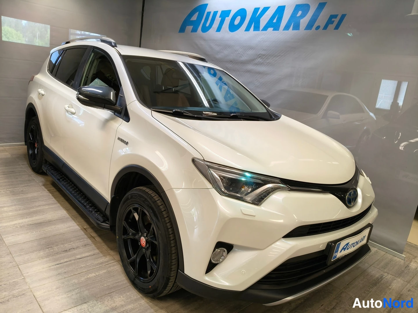 Etuviisto, nokka oikealle: Valkoinen Toyota RAV4 -maasturi kuvattu kolmannesporrakulmasta edestä vasemmalta, mustat kevytmetallivanteet ja kattokaiteet.