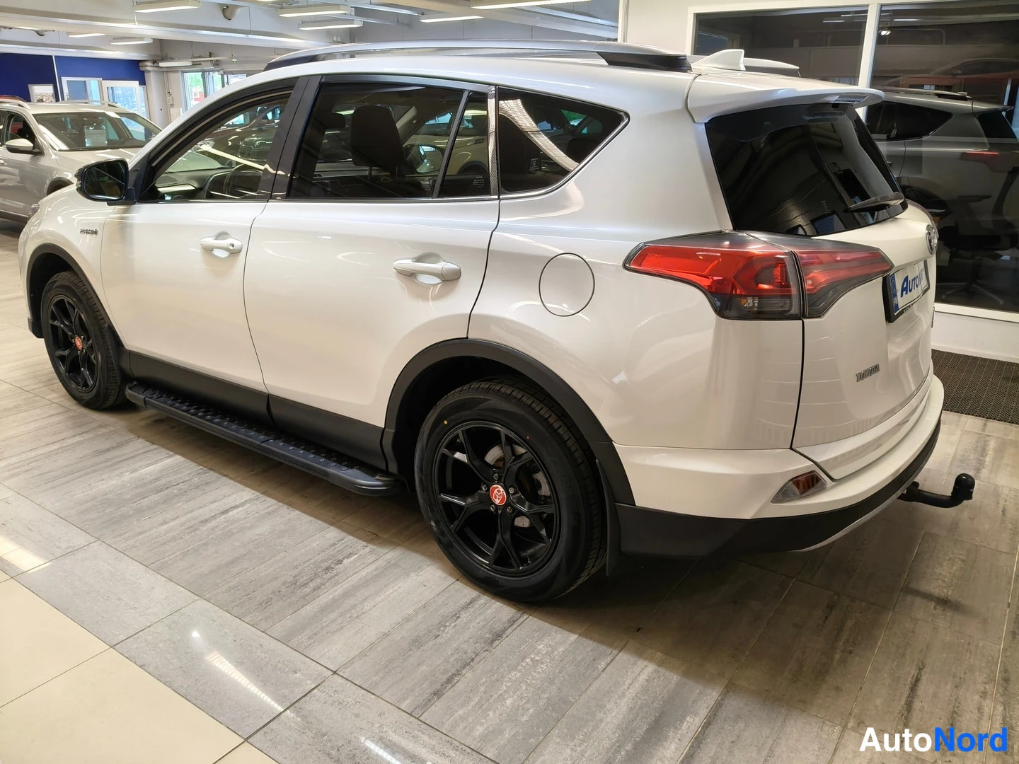 Takaviisto: Valkoisen Toyota RAV4:n takakolmannesporraskulma vasemmalta, takavalot ja mustat vanteet näkyvissä.