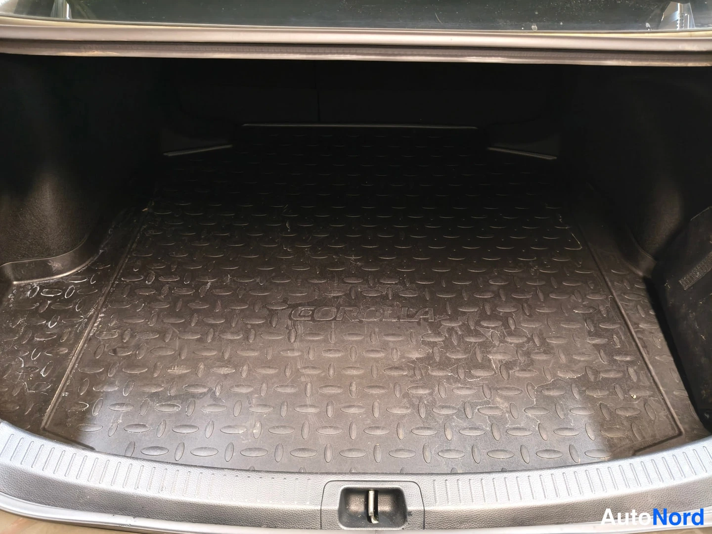 Muu: Avoimen tavaratilan pohja, jolla musta uritettu rubberimatto, jonka keskellä lukee COROLLA.