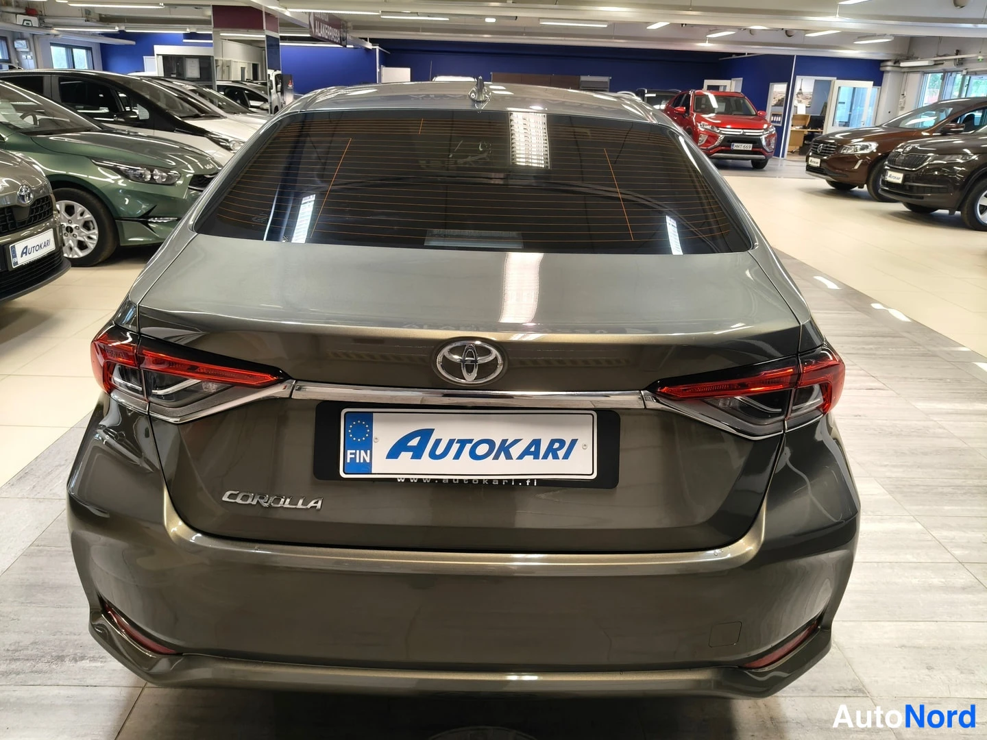 Takaa: Toyota Corolla -sedanin takapää suoraan takaa kuvattuna; auton koko runko näkyy, maalipinta tummanharmas-sprllilakka...