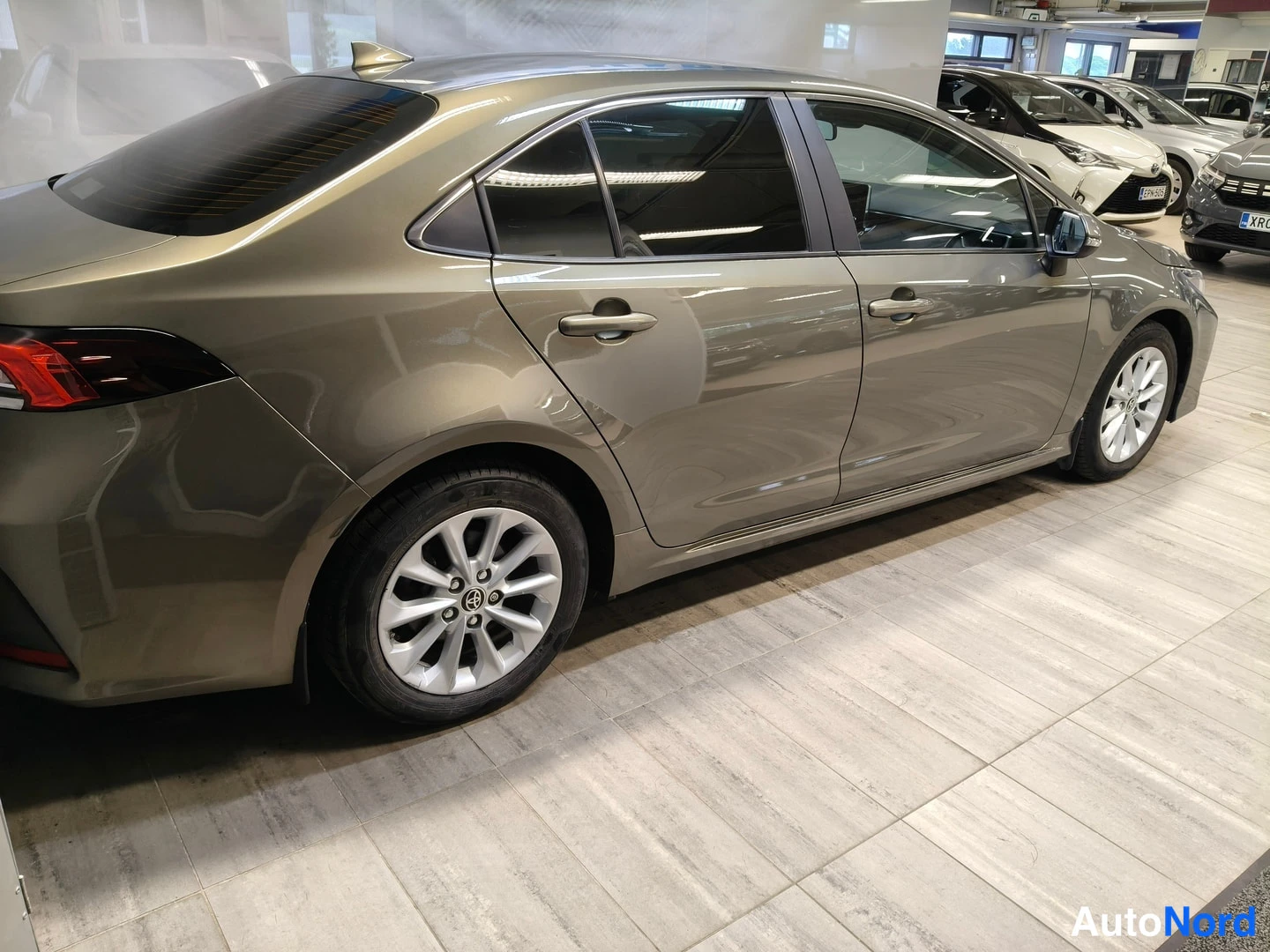 Takaviisto: Toyota Corolla -sedanin takakulma sisätiloissa, pronssinvärinen koripaneeli, takavalo ja vivut ovikahvat näkyvät.
