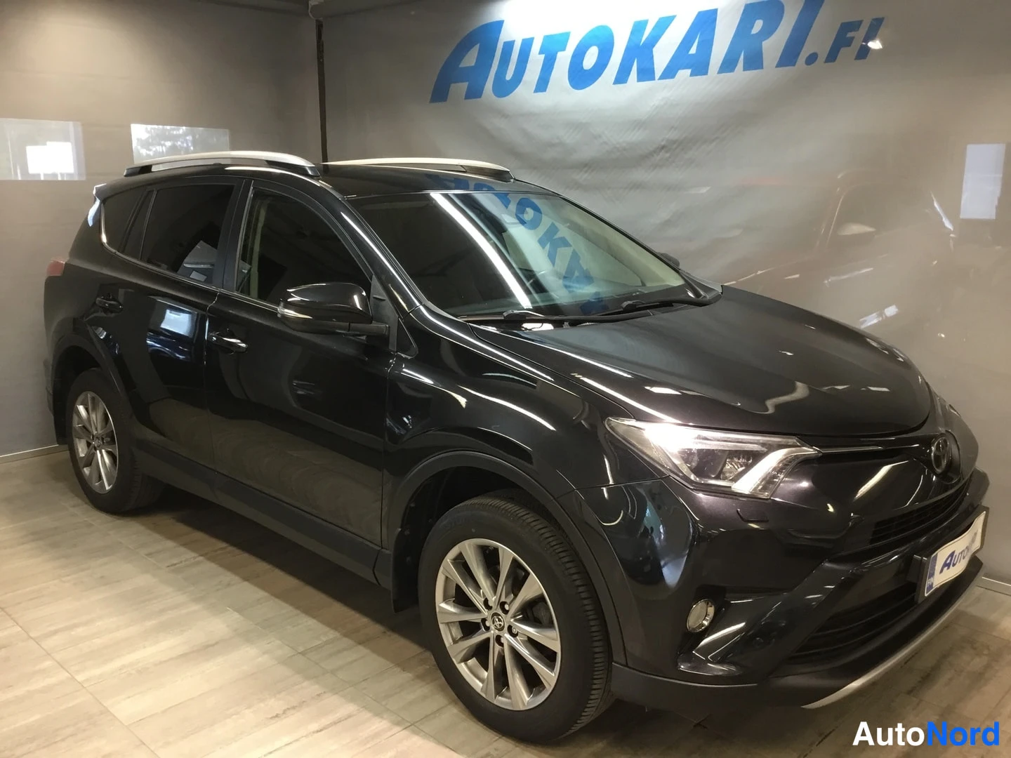 Etuviisto, nokka oikealle: Musta Toyota RAV4 etuosa vasemmalle kääntyneessä kolmannesa neljänneksestä sisätiloissa.