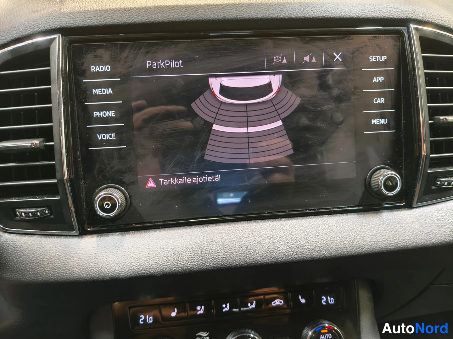 Muu: Lähikuva infotainment-näytöstä, joka näyttää ParkPilot-törmäystutkan grafiikkaa auton ympärillä ja suomenkielisen varoituksen 'Tarkkaile ajotietä!'.