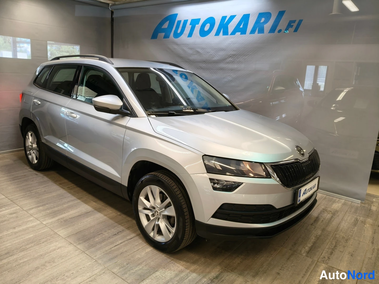 Etuviisto, nokka oikealle: Hopeanvärinen Skoda Karoq etuosa vasemmalta kolmannesnäkymässä autosalissa