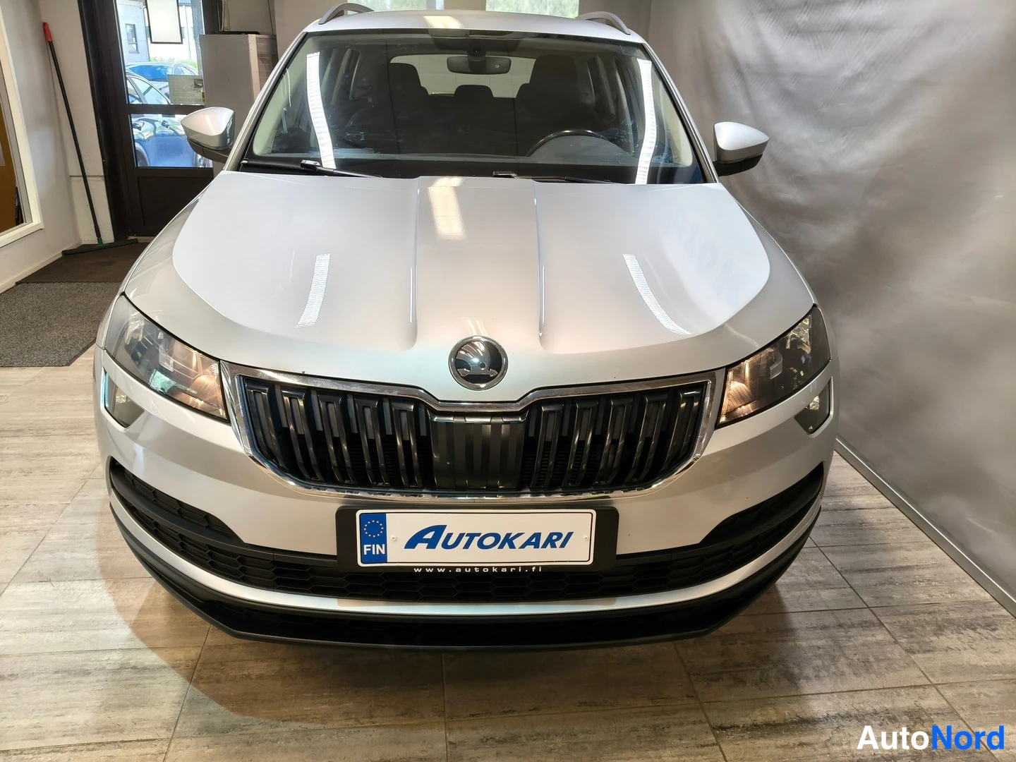 Edestä: Hopeanvärinen Skoda Karoq suoraan edestä valokuvattuna autosalissa