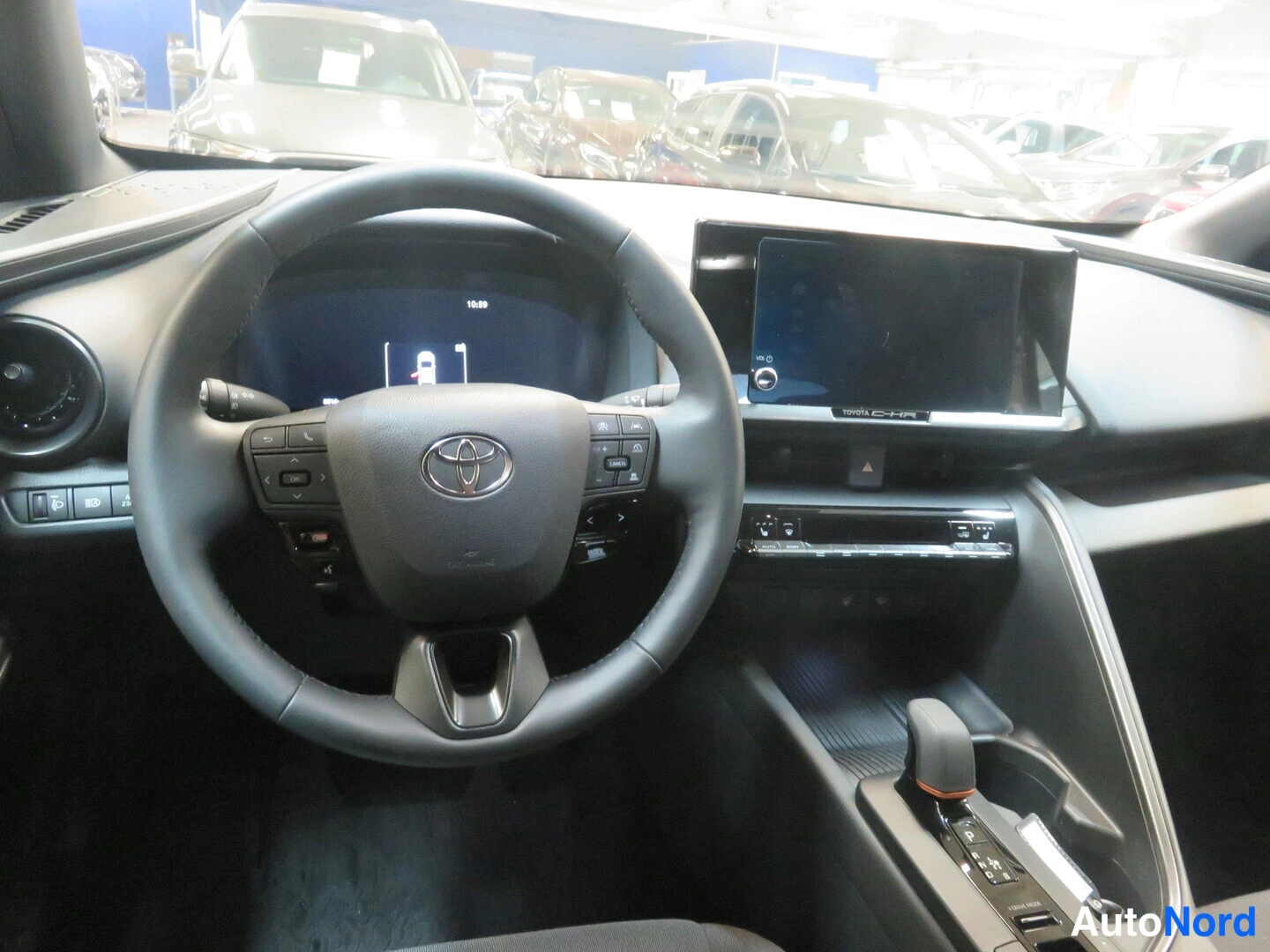 Yksityiskohta: Auton ohjaamo vasemmalta ohjattava Toyota-rattilla, keskellä kosketusnäyttö ja C-HR-teksti, oikealla vaihteenvalitsin.