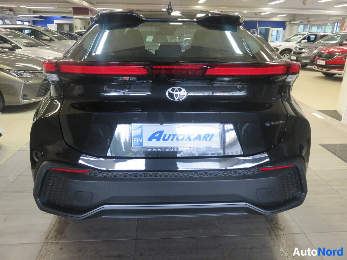 Takaa: Mustan auton perä suoraan takaa valaistussa autosalissa, Toyota-logo ja AUTOKARI-tunnus rekisterikilven paikalla.