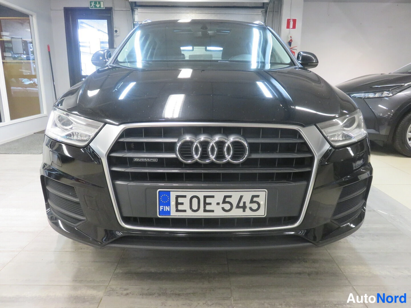 Edestä: Audi Q3:n keula suoraan edestä: musta etusäleikkö neljällä Audi-renkaalla ja quattro-tekstillä, ajovalot ja rekisterikilpi E0E-545.