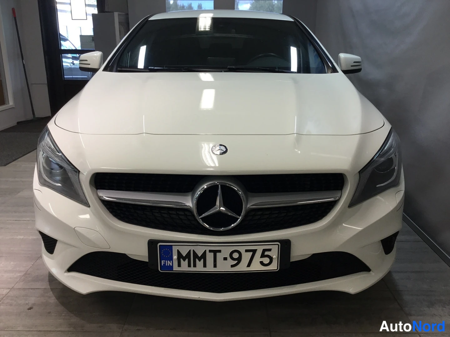 Edestä: Valkoisen Mercedes-Benzin keula suoraan edestä, näkyvät Mercedes-tähti etusäleikössä, etulyhdyt ja rekisterikilpi.