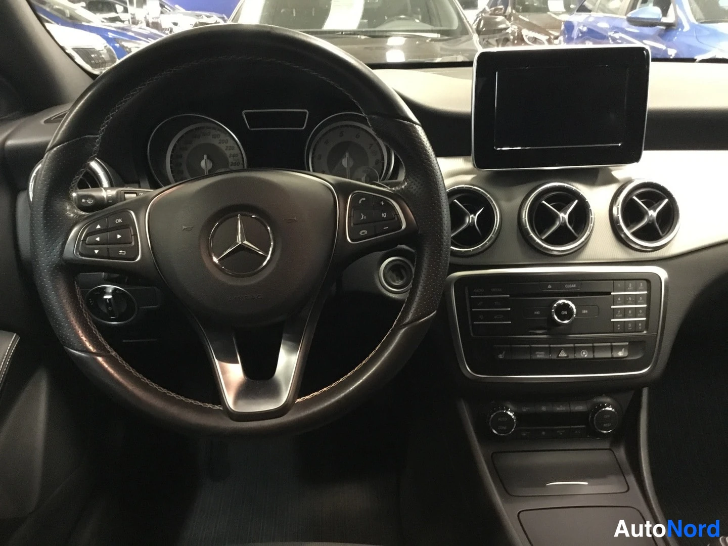 Edestä: Mercedes-Benzin ohjaamosta: Mercedes-merkillinen ratto, mittaristo ja keskikonsolissa palautusneste- ja ilmastointipainikkeet.