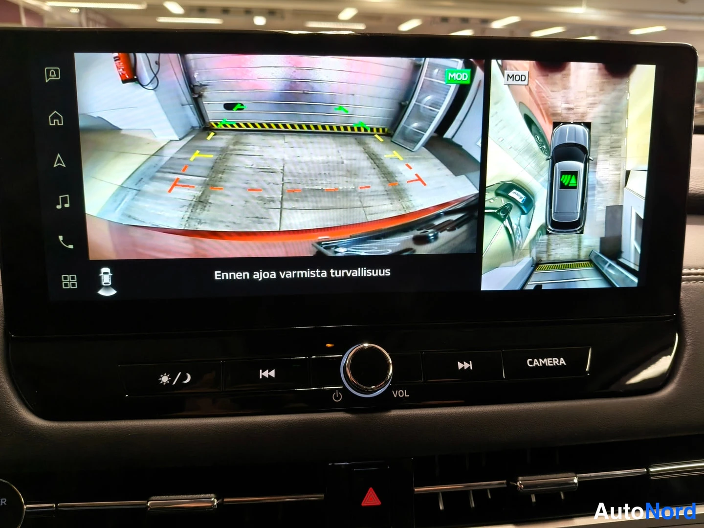Muu: Infotainment-näytössä käytössä 360-asteinen ympäriview-kamera: etunäkymä varastotilasta ja lintuperspektiivinäyttö autosta, teksti Ennen ajoa varmista turvallis