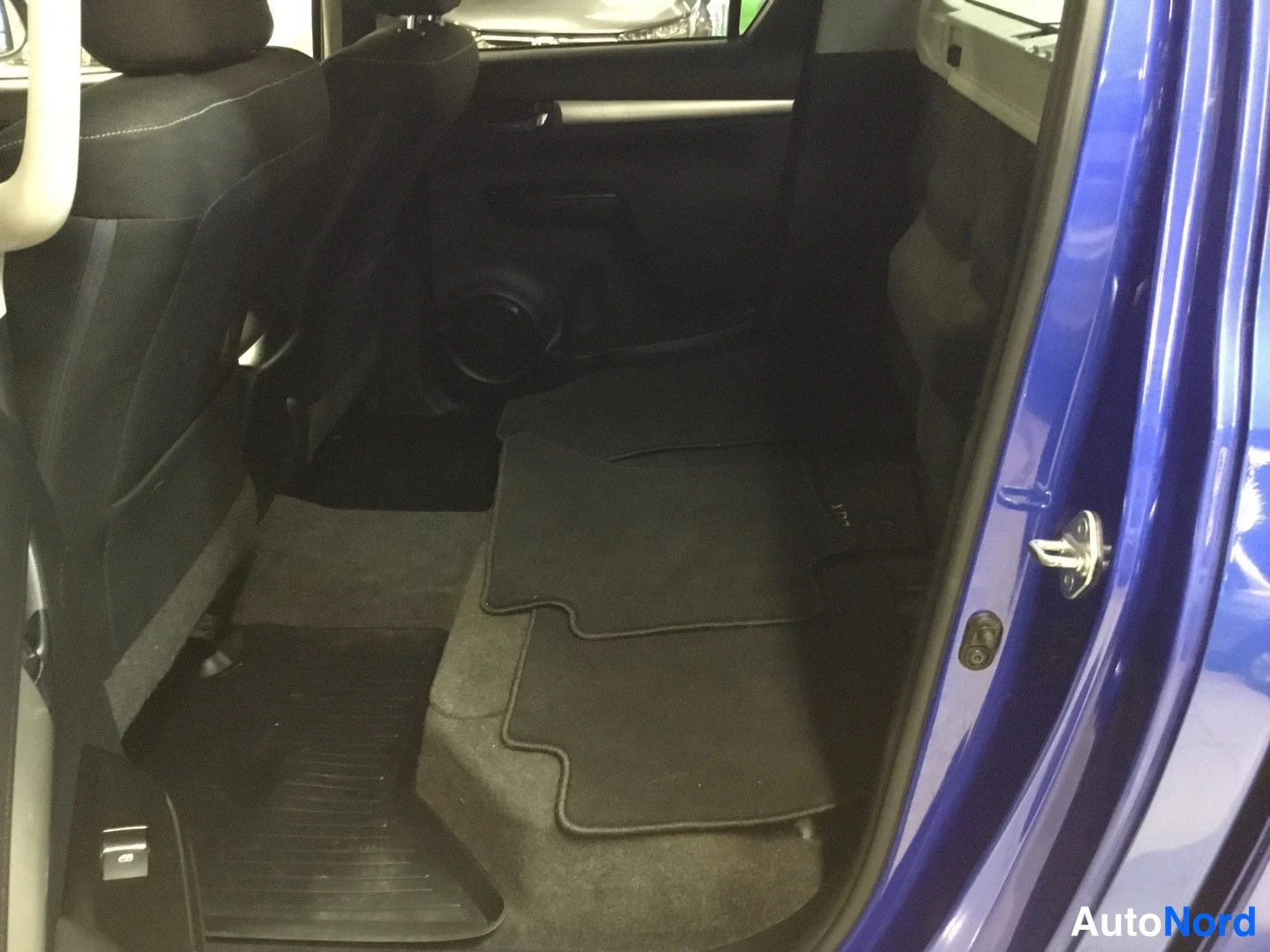 Muu: Toyota Hiluxin takaistuimet kuvattuna avatusta takaovesta: tummat istuimet, ovenkarmi on sininen.