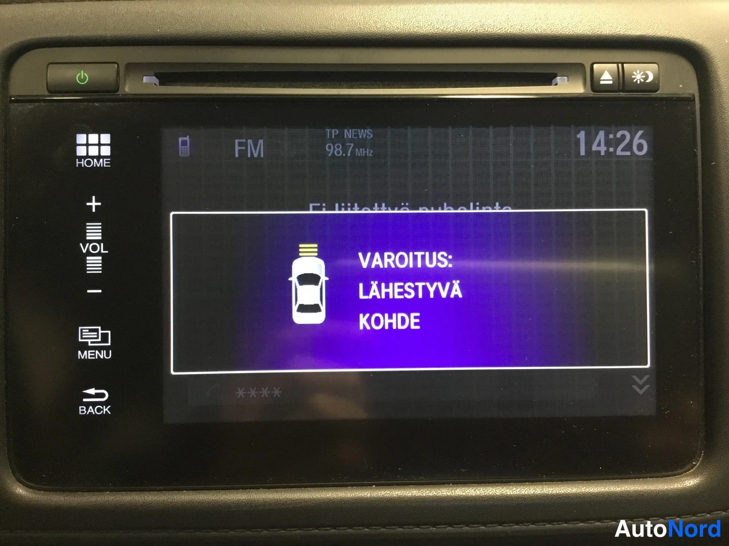 Muu: Auton kosketusnäytön varoitus 'VAROITUS: LÄHESTYVÄ KOHDE', radio kanavalla FM 98.7 MHz kello 14:26.