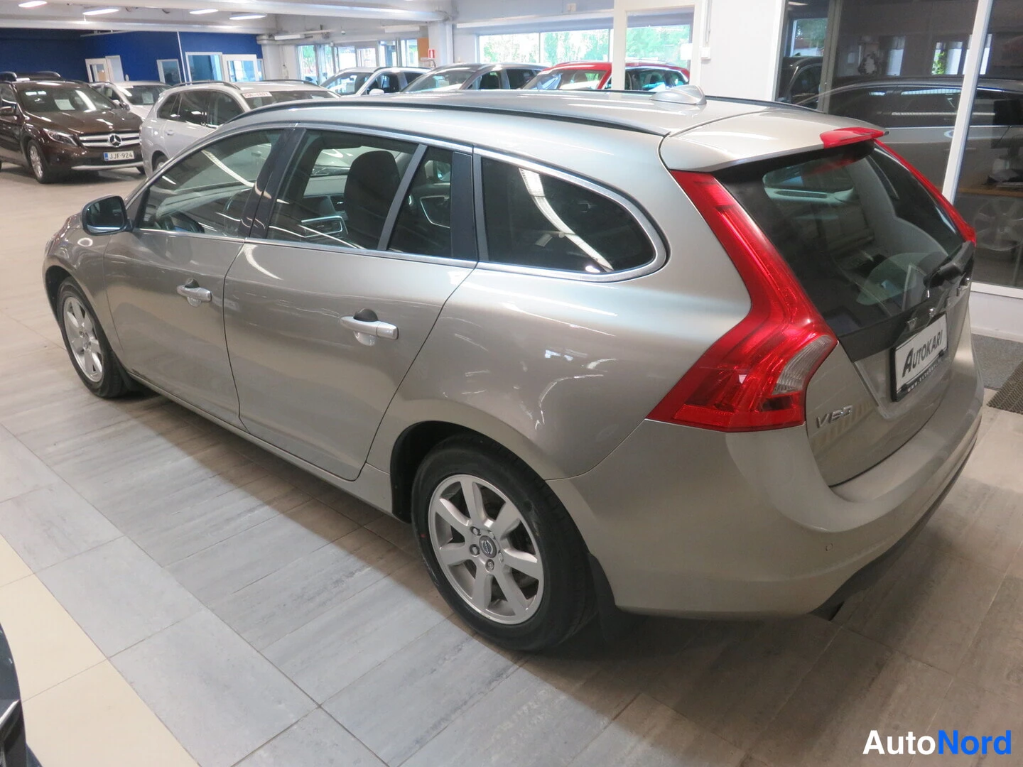 Takaviisto: Volvo V60 -farmari takaa viistosti sisätiloissa, hopeanvälinen korimalli ja punaiset takavalot näkyvät.
