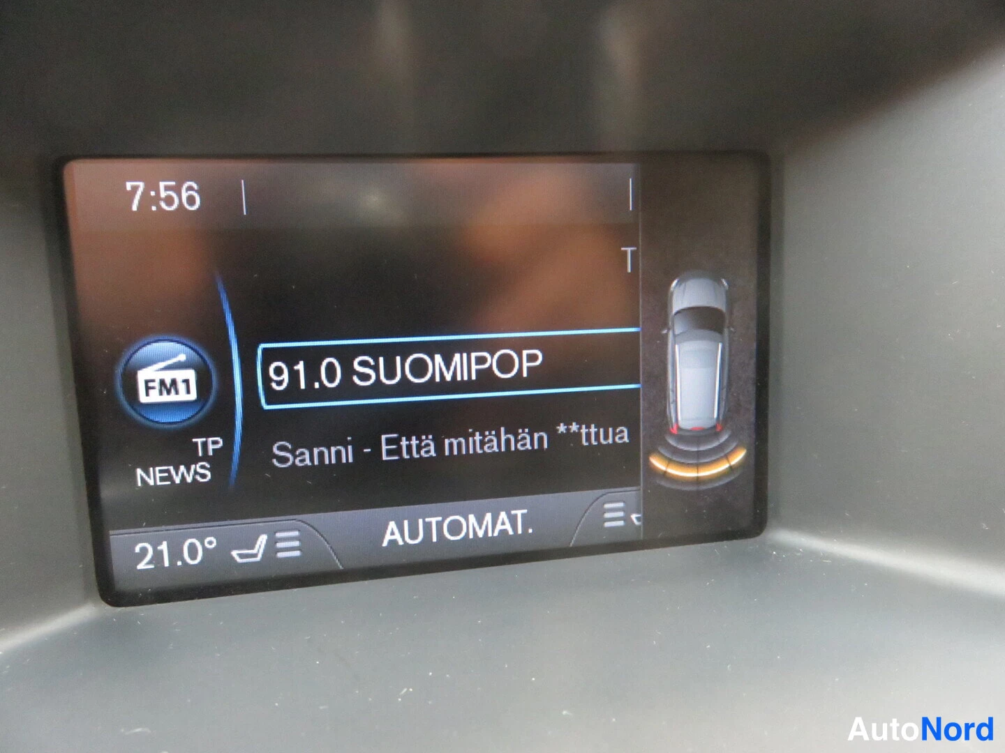 Muu: Auto infiniti-navin näyttö: radio kanava 91.0 SUOMIPOP, kello 7:56 ja pysäköintitutkan grafiikka.