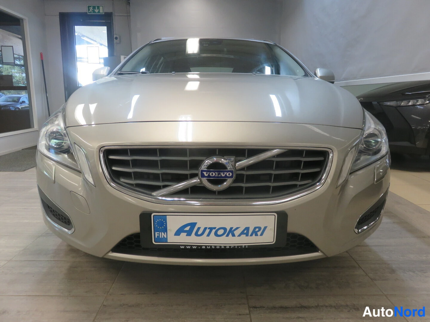 Edestä: Volvo V60:n etupää suoraan edestä, Volvo-merkki säleikössä ja Autokari-kilpi etupuskurin rekisterinumeron paikalla.