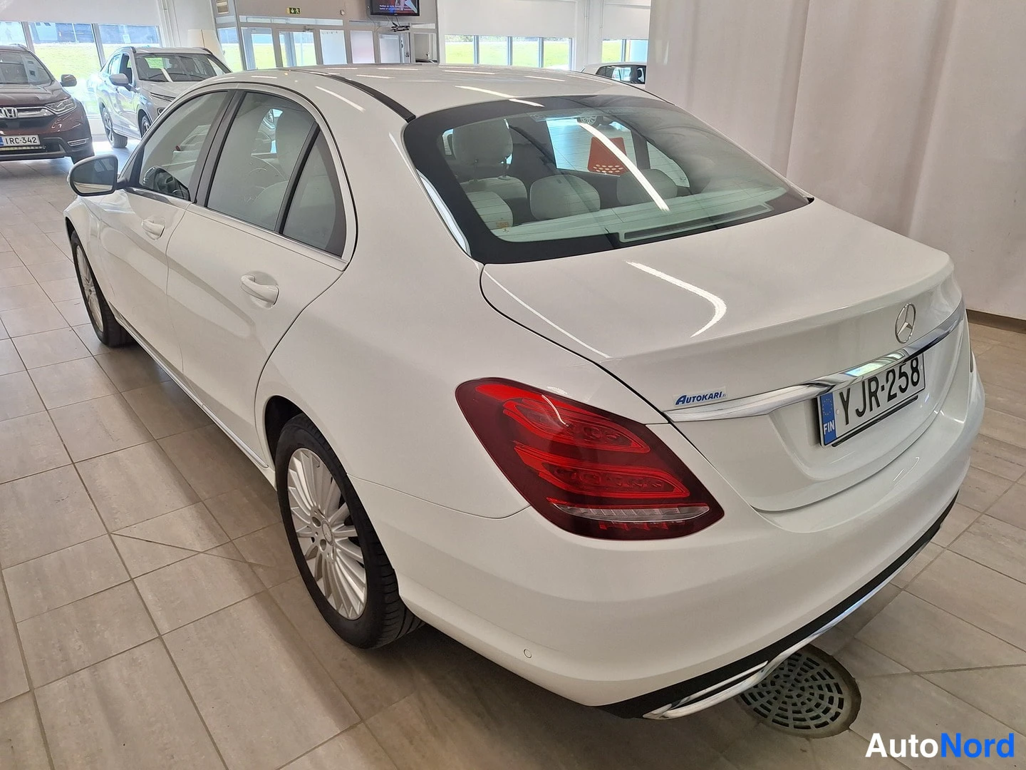 Takaviisto: Valkoinen Mercedes-Benz C-sarjan sedan takaviistosta vasemmalta, rekisterikilpi Y JR-258 ja Autokari-tarra takaluukussa.