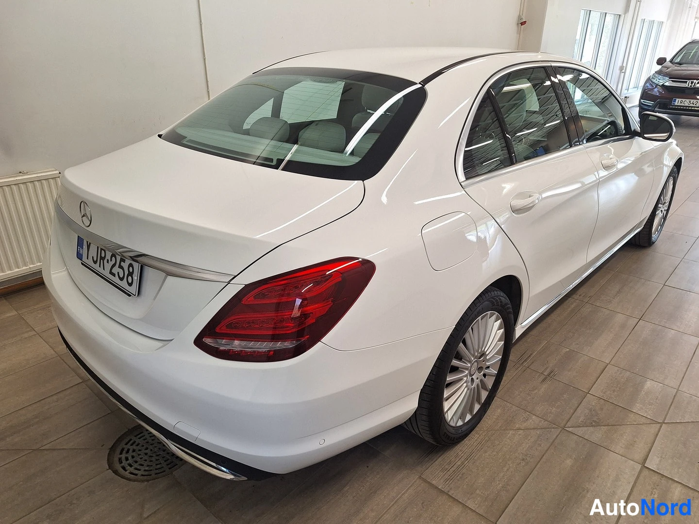Takaviisto: Valkoinen Mercedes-Benz C-sarjan sedan takaviistosta oikealta, rekisterikilpi Y JR-258, sisätiloissa laatoitetulla lattialla.
