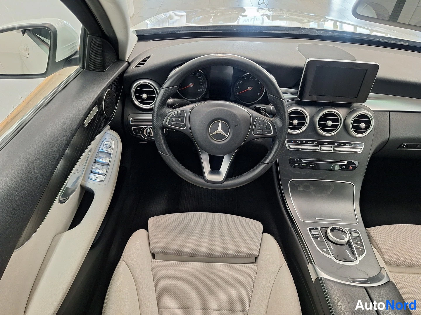 Edestä: Mercedes-Benzin ohjaamo: ohjauspyörä, mittaristo, keskinäyttö ja vaalea kuljettajan istuin.