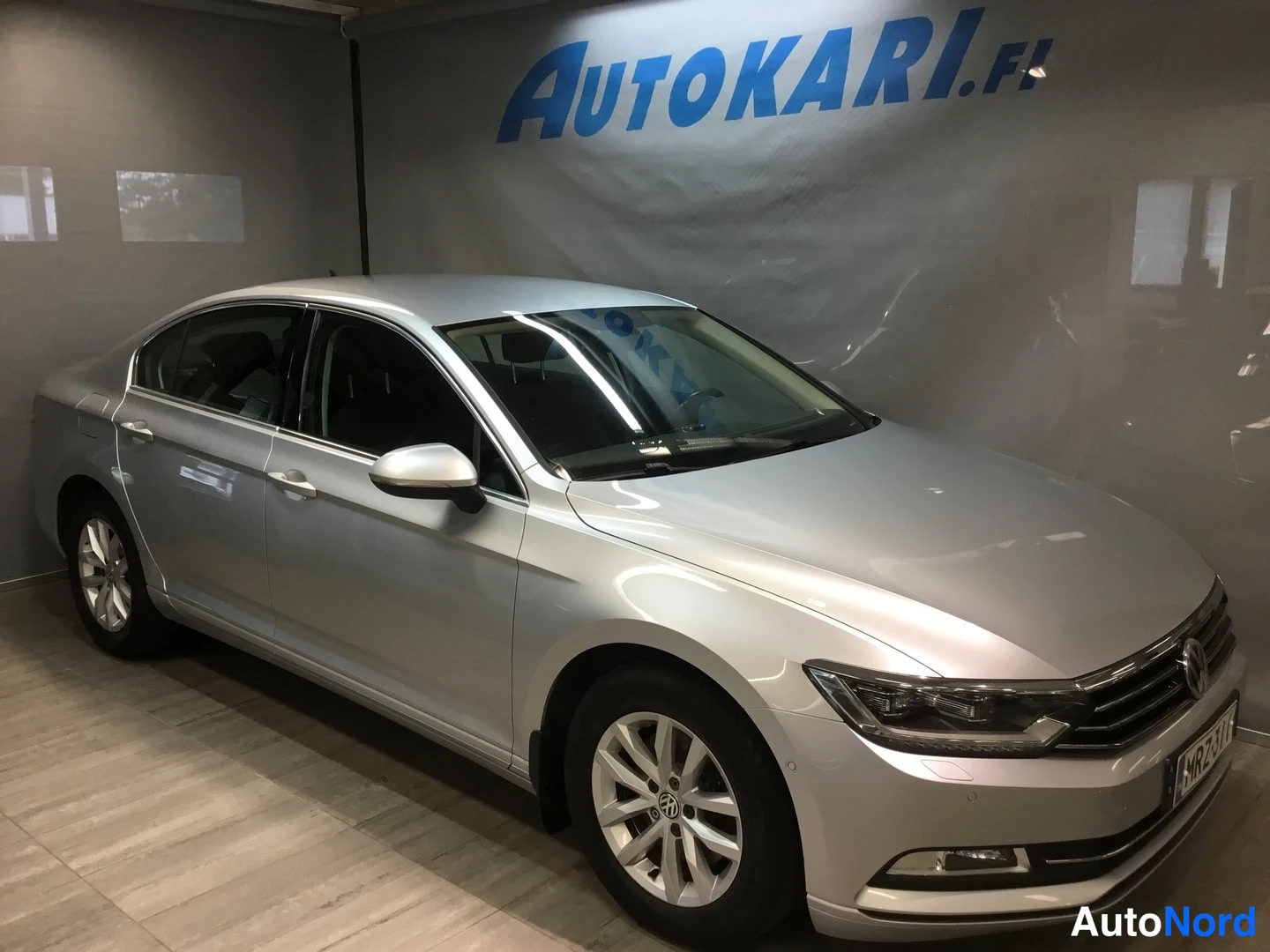 Etuviisto, nokka oikealle: Hopeanvärinen Volkswagen Passat -sedan esillä sisätilassa, kolme neljäsosaa edestä oikealta.