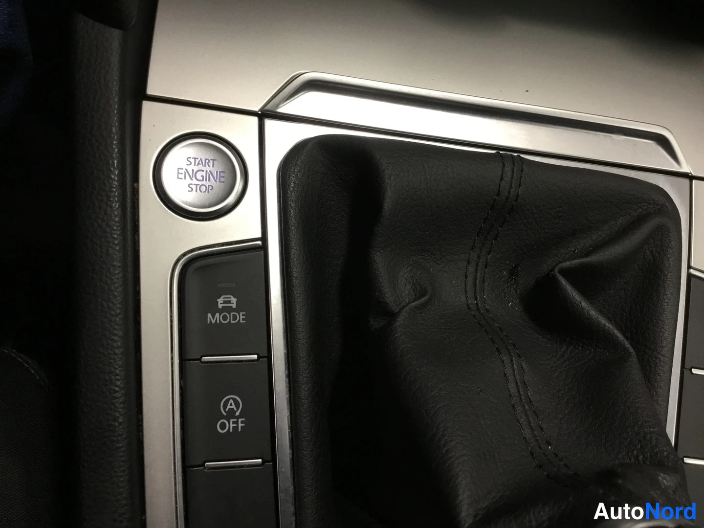 Yksityiskohta: Sisätilakuvan yksityiskohta: START ENGINE STOP -käynnistysnappi, MODE-nappi ja A OFF -nappi keskikonsolissa.