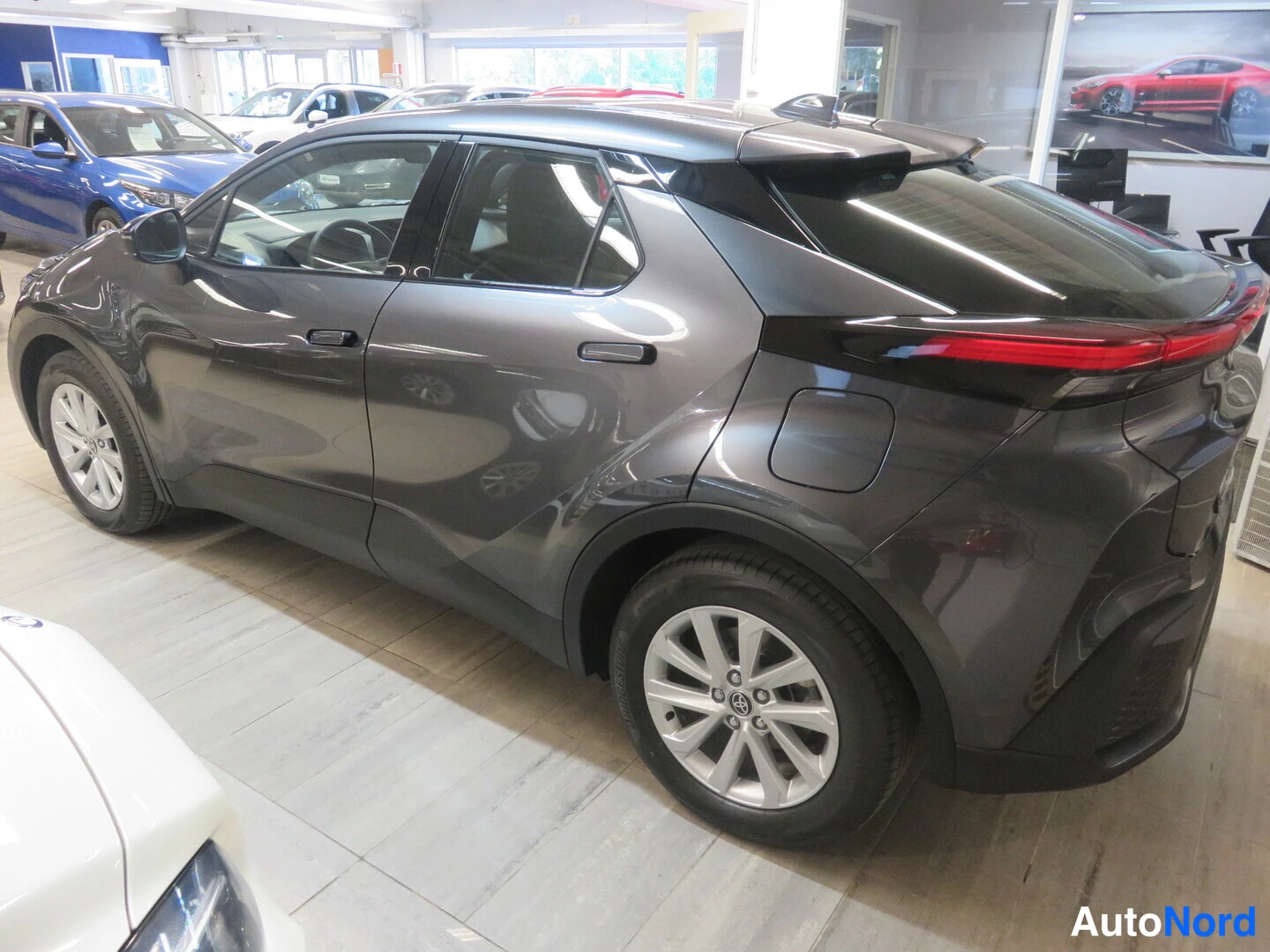 Takaviisto: Tummanharmaa Toyota C-HR takavasemmasta kolmivartinäkymässä autosalon lattialla.