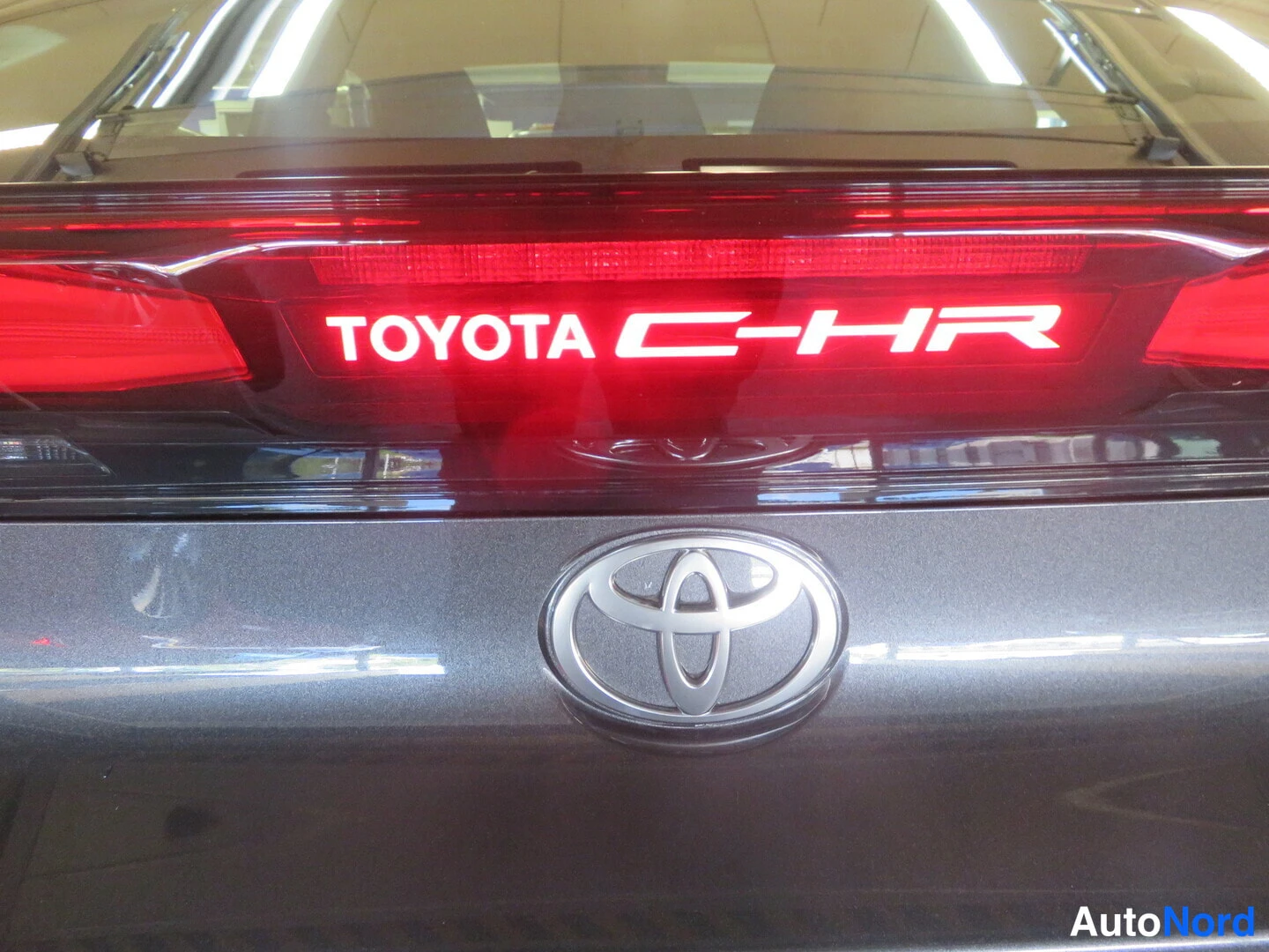 Takaa: Lähikuva Toyota C-HR:n takavaloiskusta, jossa valkoinen TOYOTA C-HR -teksti, ja Toyota-embleemistä perässä.