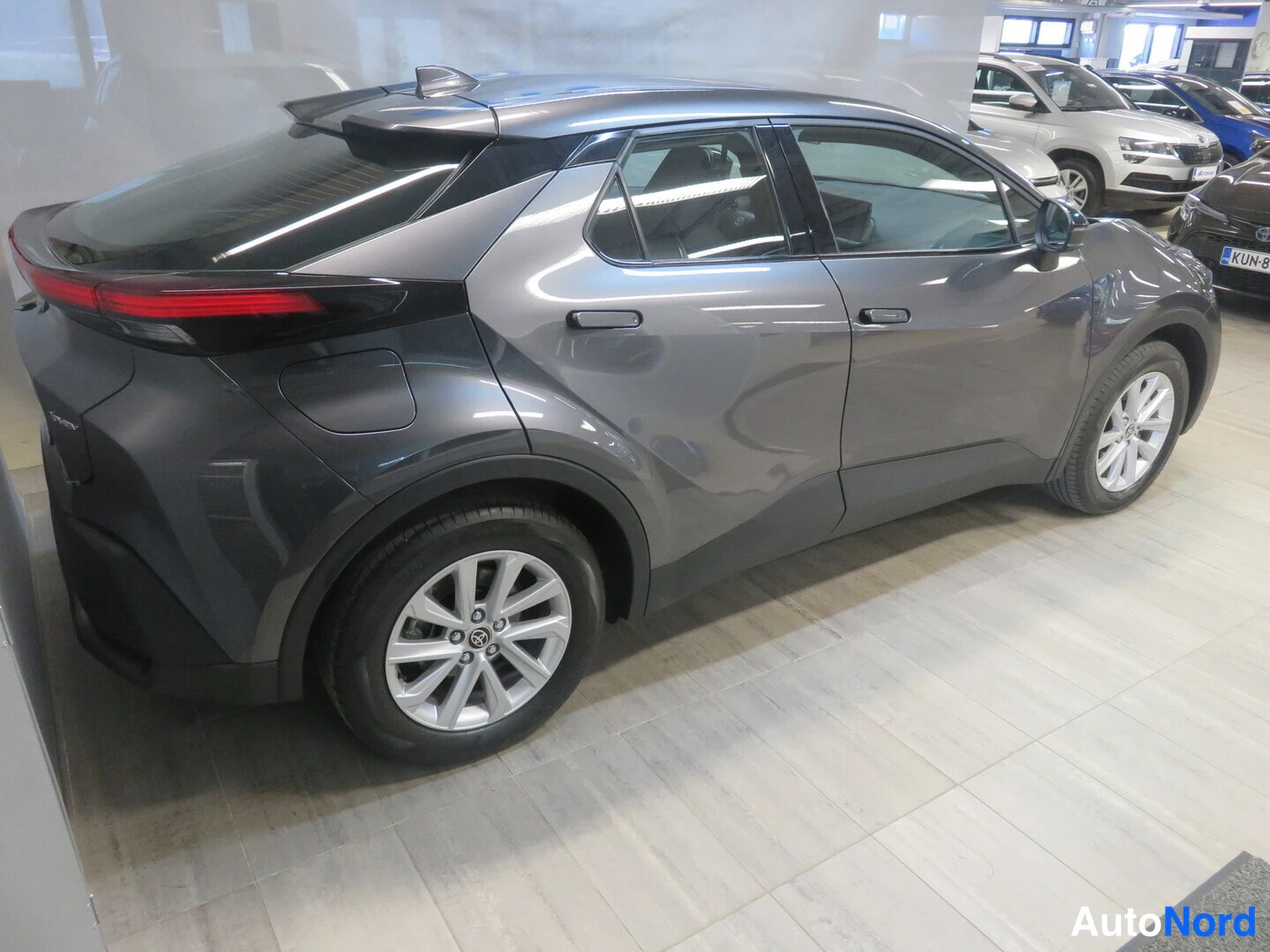 Takaviisto: Tummanharmaa Toyota C-HR takavasemmasta kolmivartinäkymässä autosalon lattialla.