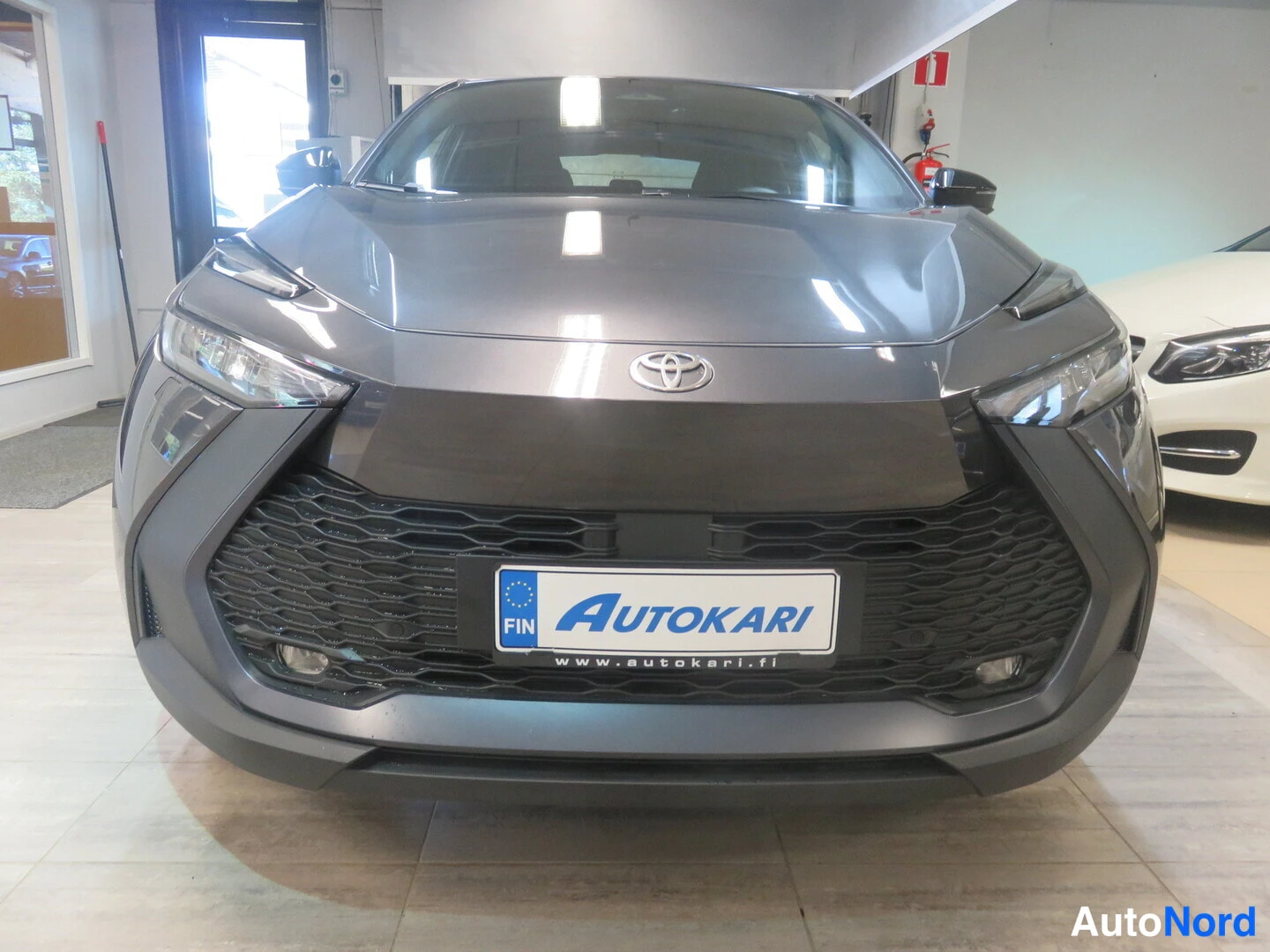 Edestä: Auton suora etunäkymä, tummanharmaa etupaneeli ja Toyota-merkki näkyvät.