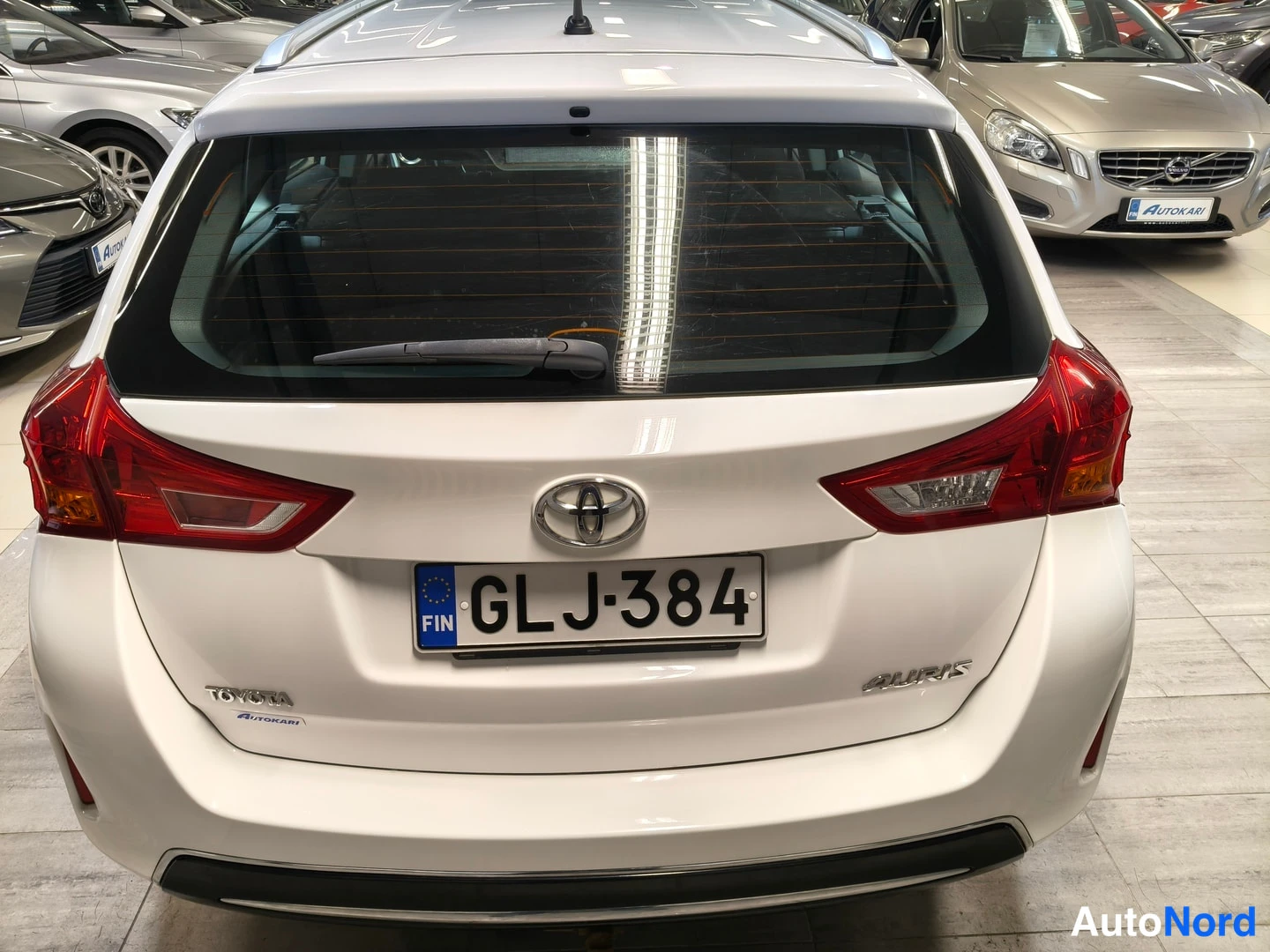 Takaa: Takaa kuvattu valkoinen Toyota Auris -farmari, rekisteritunnus, myymälän sisätiloissa.