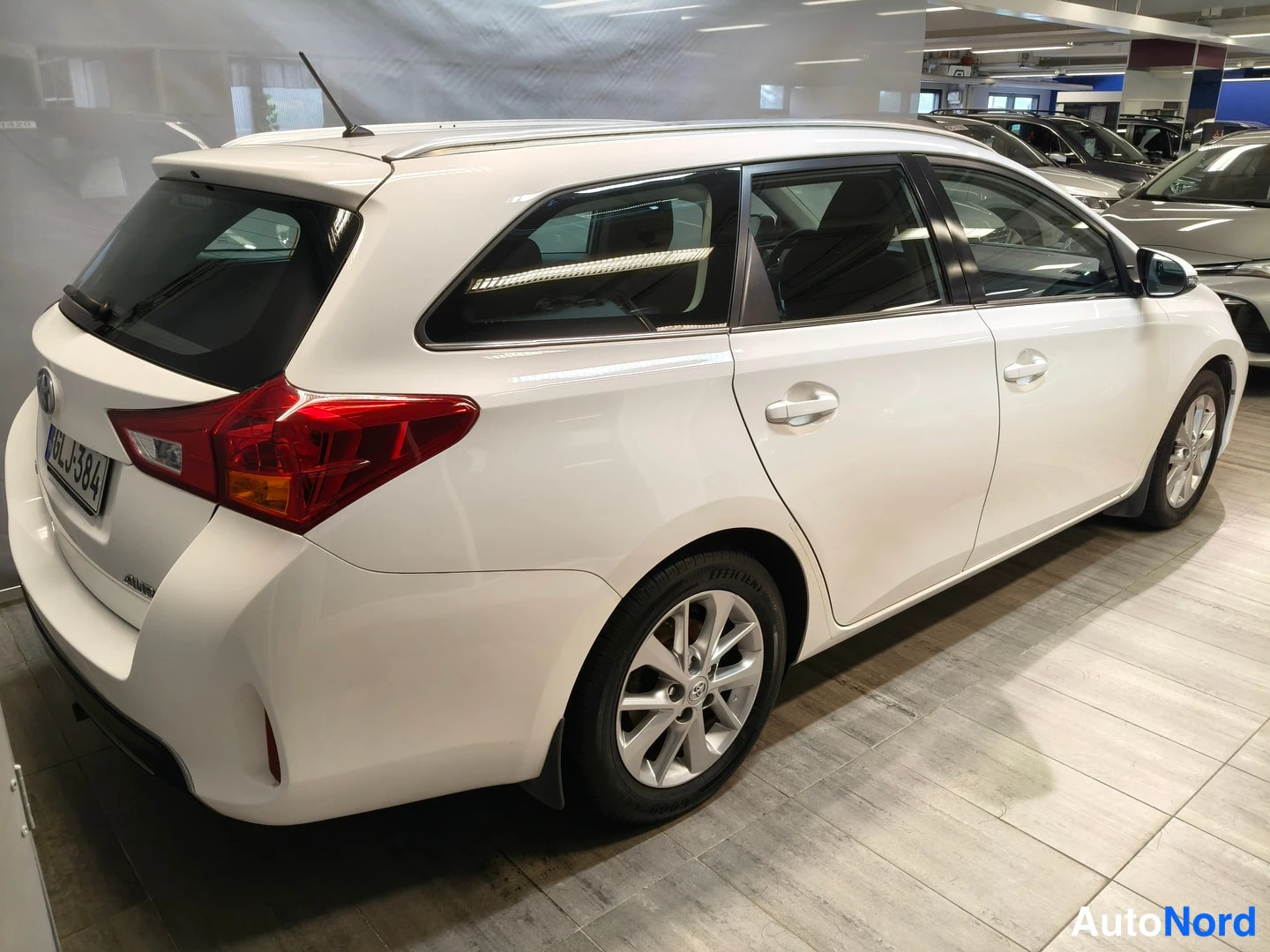 Takaviisto: Takanurkkakuvassa valkoinen Toyota Auris -farmari sisätiloissa, koko ajoneuvo näkyvissä.