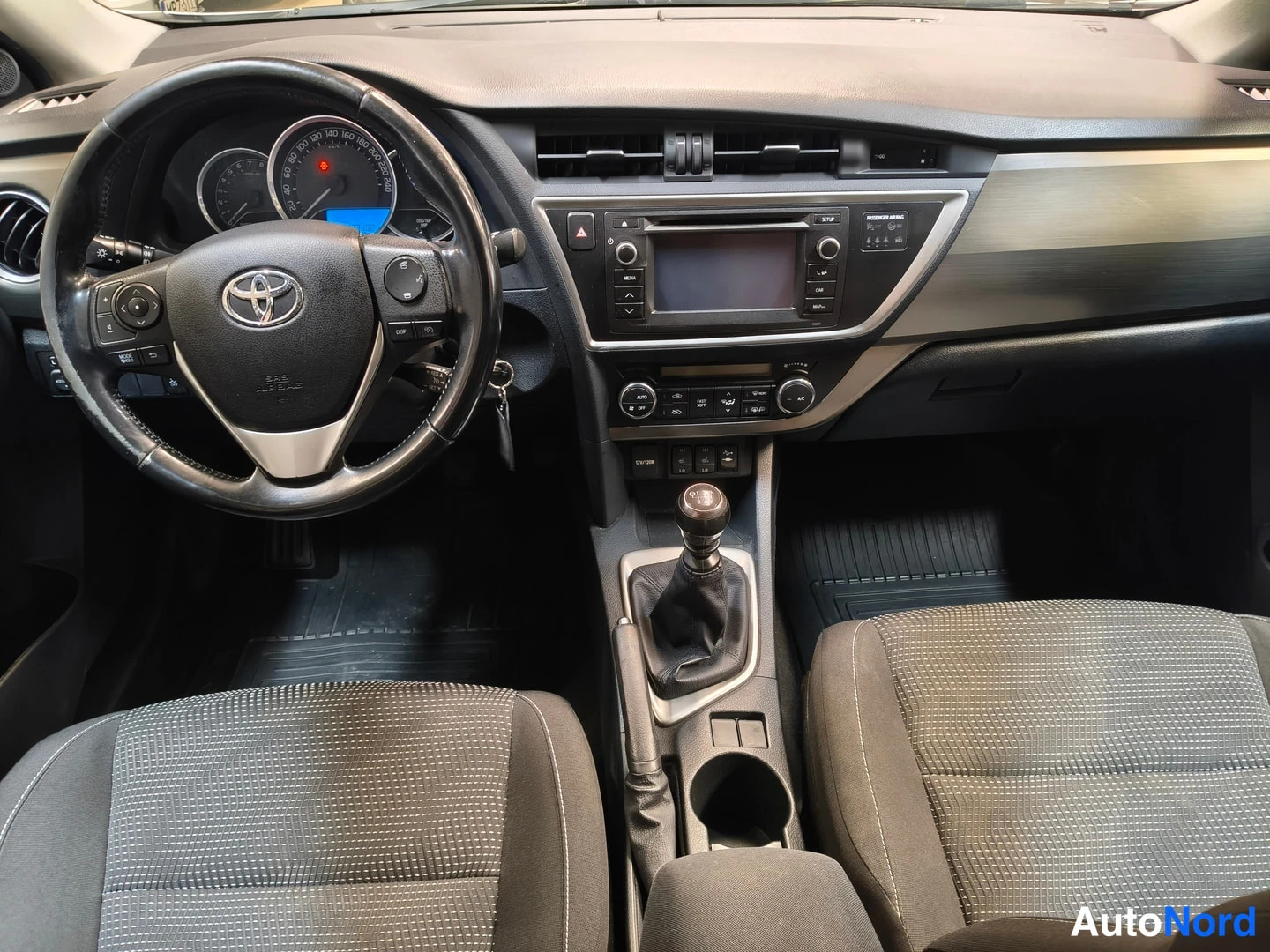 Muu: Ohjaamo edestä: Toyota-ohjauspyörä, analogiset mittarit, manuaalivaihtoerin ja kankaanpenkit.
